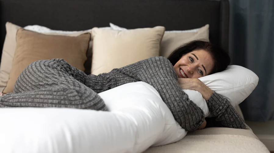 A woman hugs a long body pillow, part of the Sleep Again Pillow System.