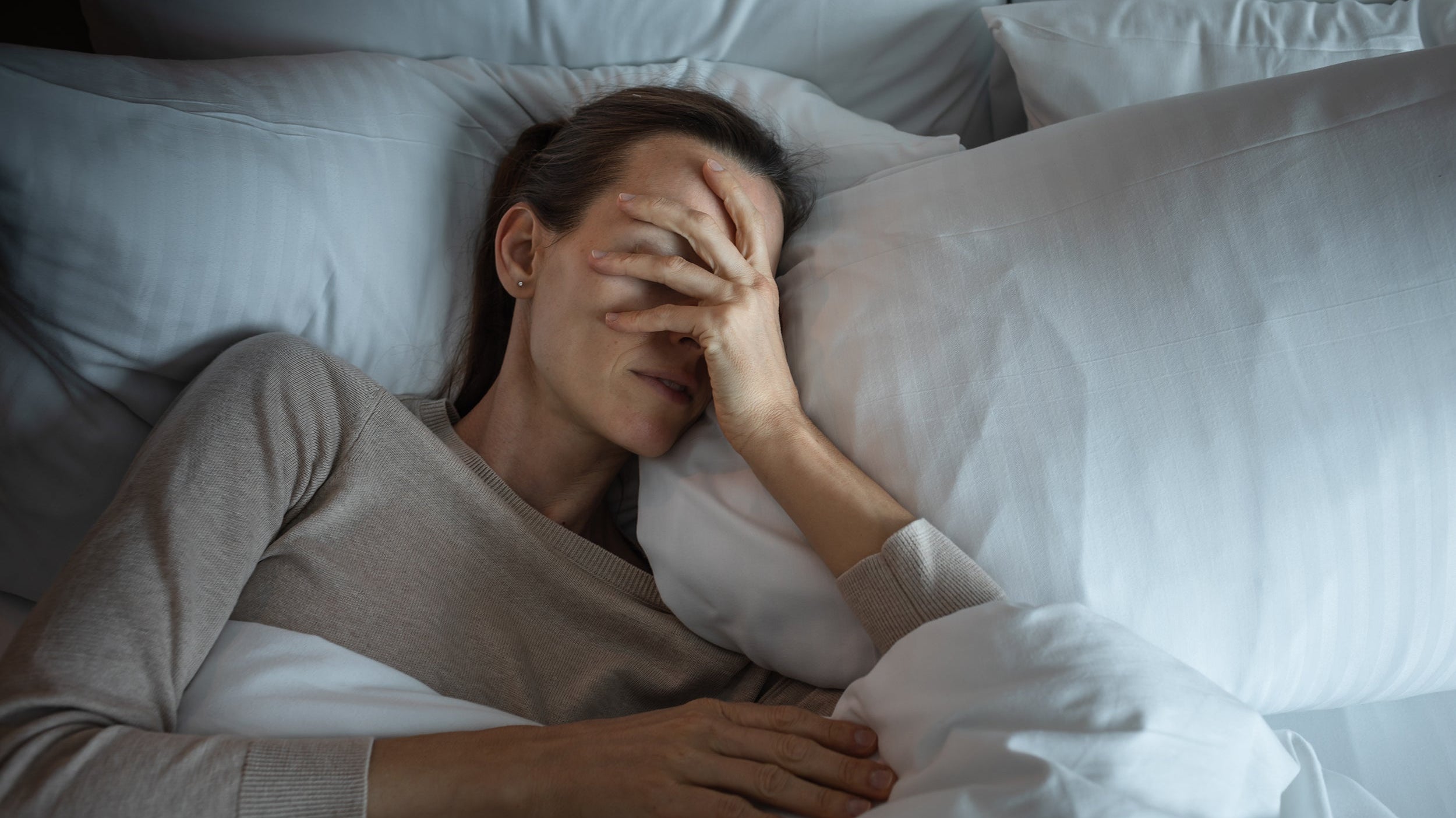 A woman struggles to sleep. Learn more on how to stop rolling over onto your back following breast surgery in our complete guide.