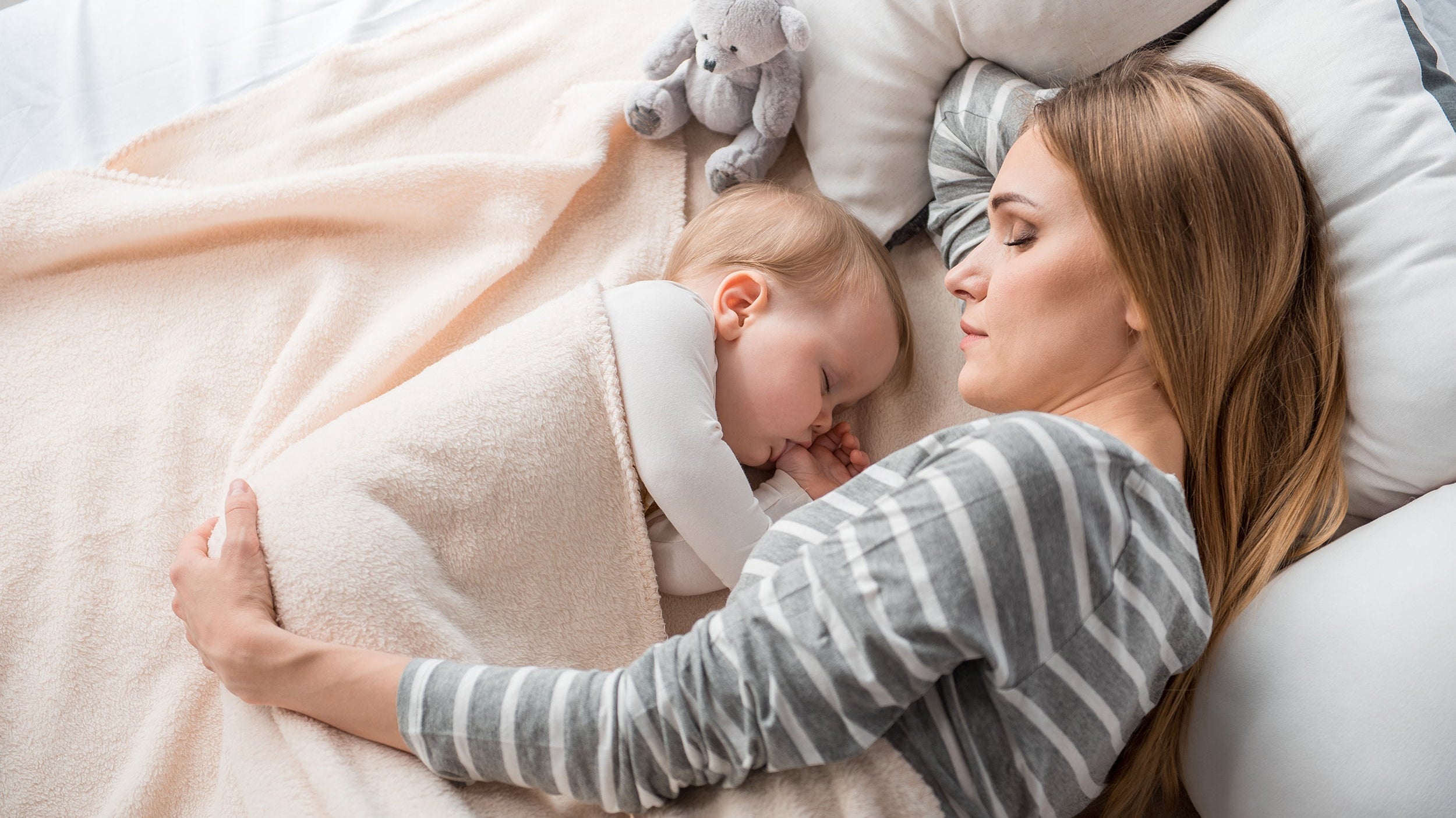 A mother and her newborn baby rest in bed. Sleeping after a C-section can be challenging. Learn more about real solutions for how to sleep after C-section in our new mom survival guide.