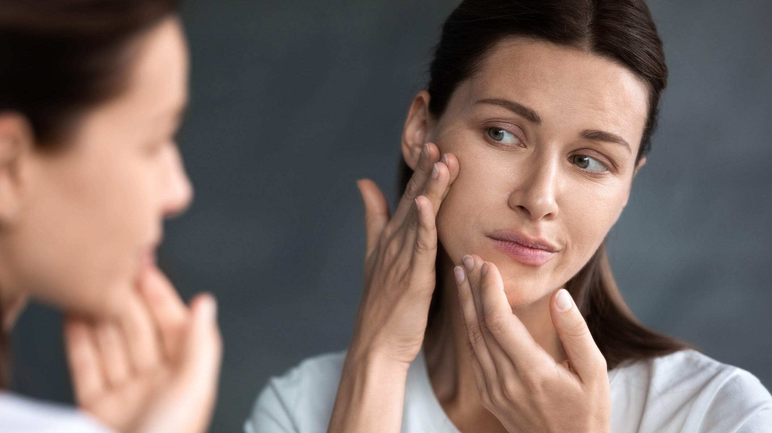 A woman looks at her face in the mirror. Elevated back sleeping at 30–45 degrees is the key to managing swelling after genioplasty. Here's how to maintain it all night without stacked pillows.