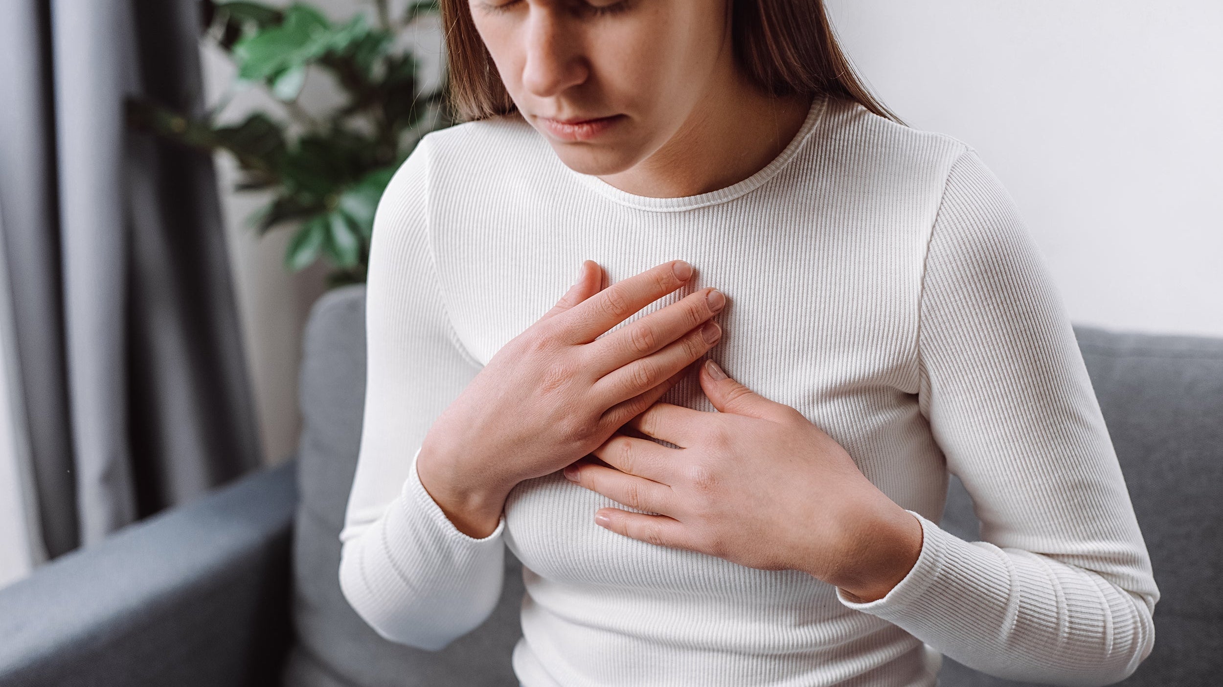 A woman clutches her chest. Tired of waking up with burning chest pain? Learn the best sleep positions and elevation techniques to stop nighttime acid reflux and finally sleep peacefully.