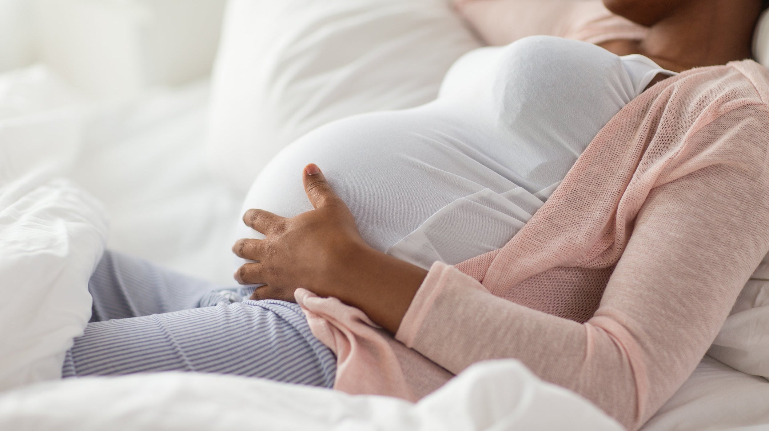 A pregnant woman rests in bed. Learn how to use a pregnancy pillow in our comprehensive guide and get the nurturing sleep you and your growing baby deserve.