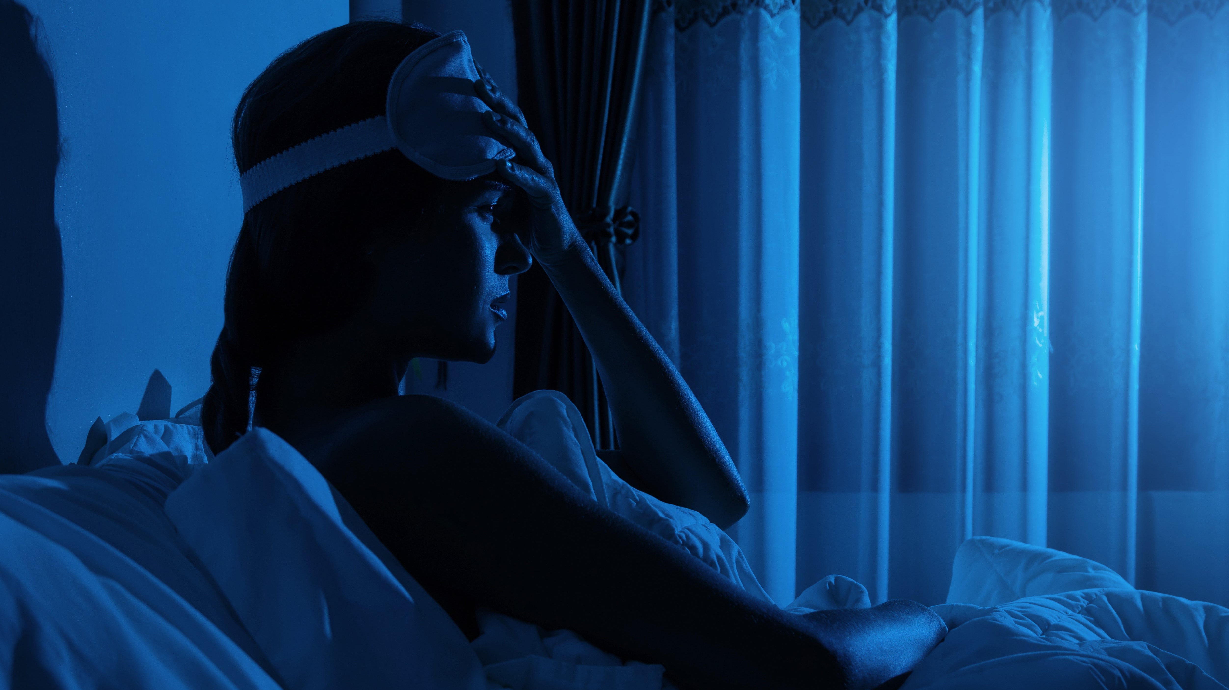 A woman struggles with insomnia while in bed. Insomnia after surgery is extremely common. Get the healing rest you need and deserve in our full guide.