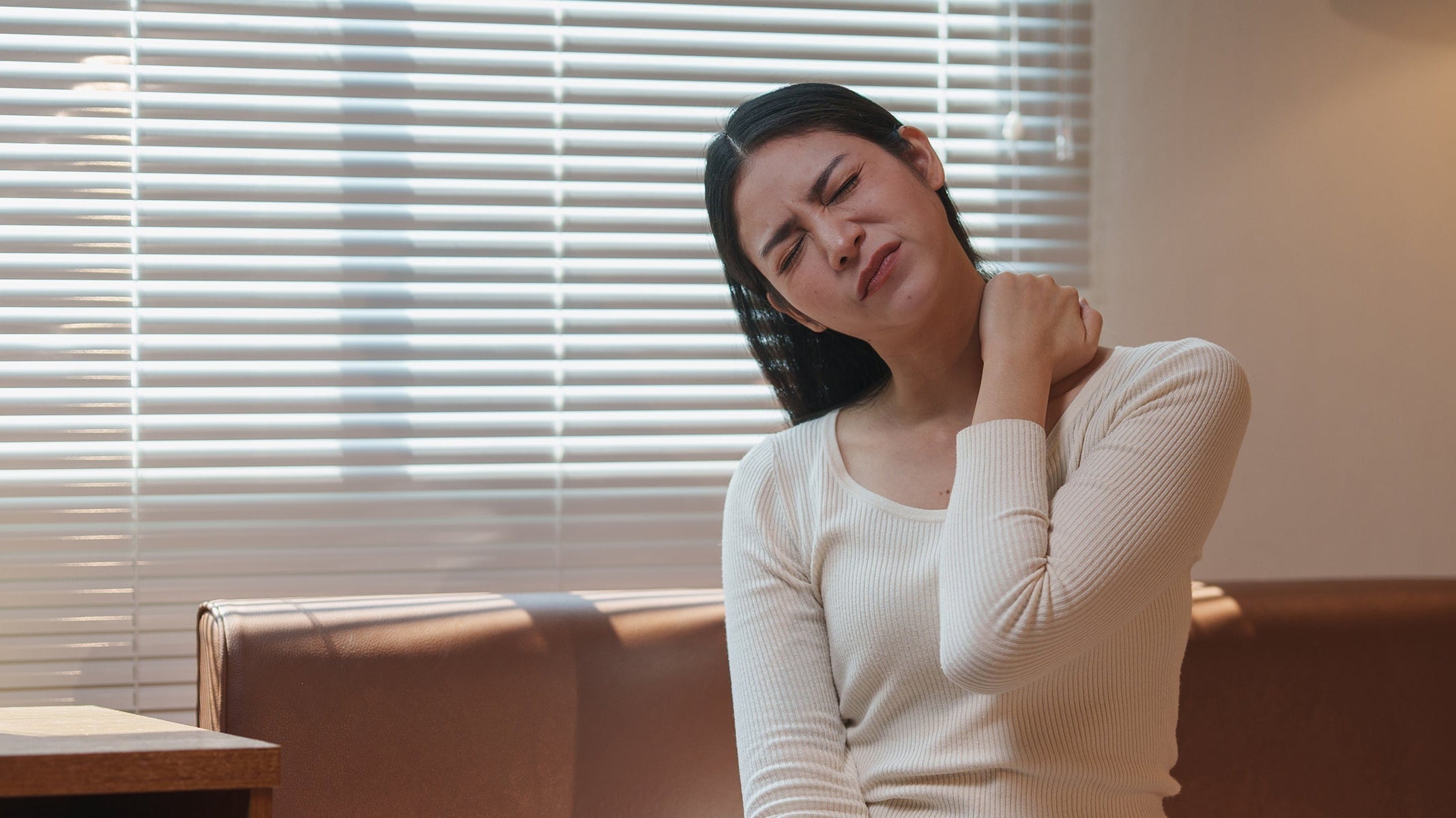 A woman clutches her neck in pain. If you're experiencing rhomboid pain, learn how your sleep position can help.