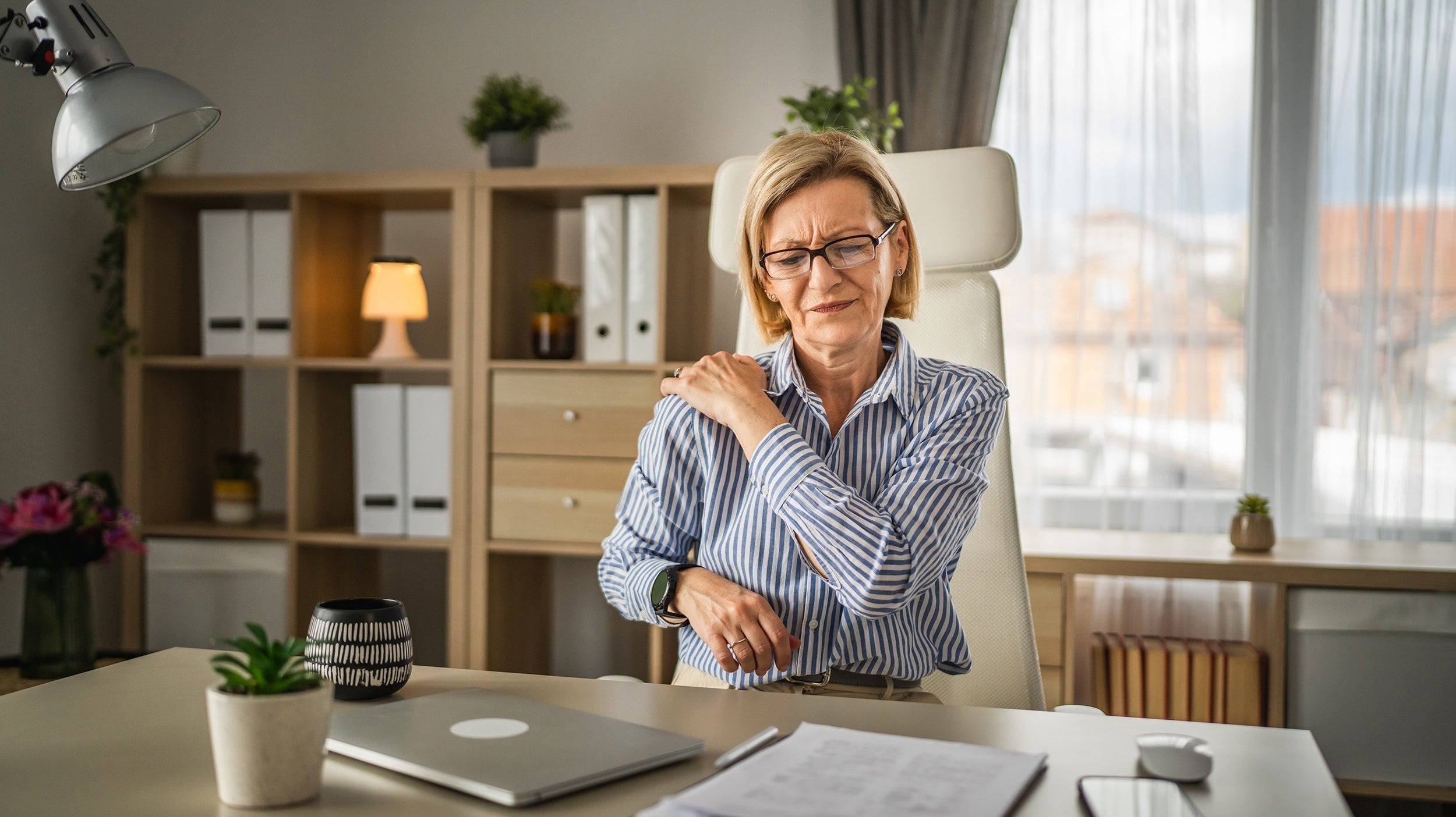 A woman clutches her shoulder in pain. Getting good sleep after shoulder can be extremely challenging. Learn which sleeping positions after shoulder surgery can help you maximize recovery in our comprehensive guide.