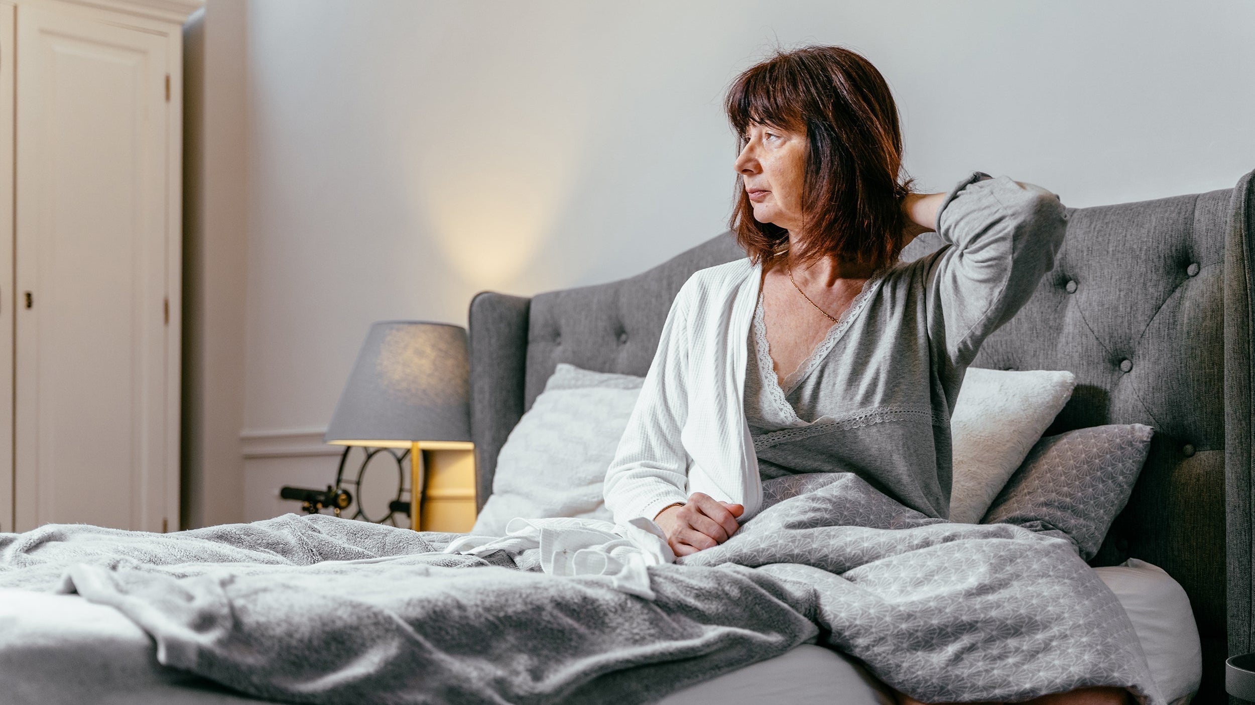 A woman sits up in bed. How to sleep comfortably with tissue expanders: proper elevation angles, safe side sleeping transitions, and positioning support that adapts as expanders fill.