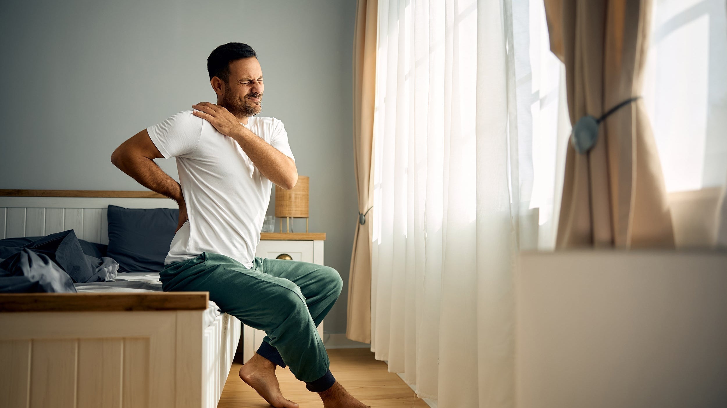 A man clutches his upper shoulder in bed. Discover the best sleeping position for Thoracic Outlet Syndrome and actually get some rest without waking up with numb arms.