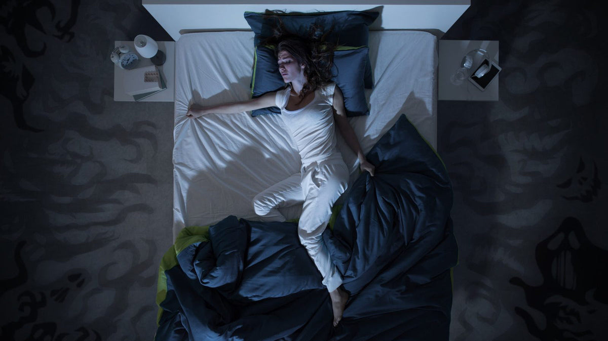 Woman lying awake in bed at night, looking uncomfortable with tangled bedding, unable to sleep because of night sweats