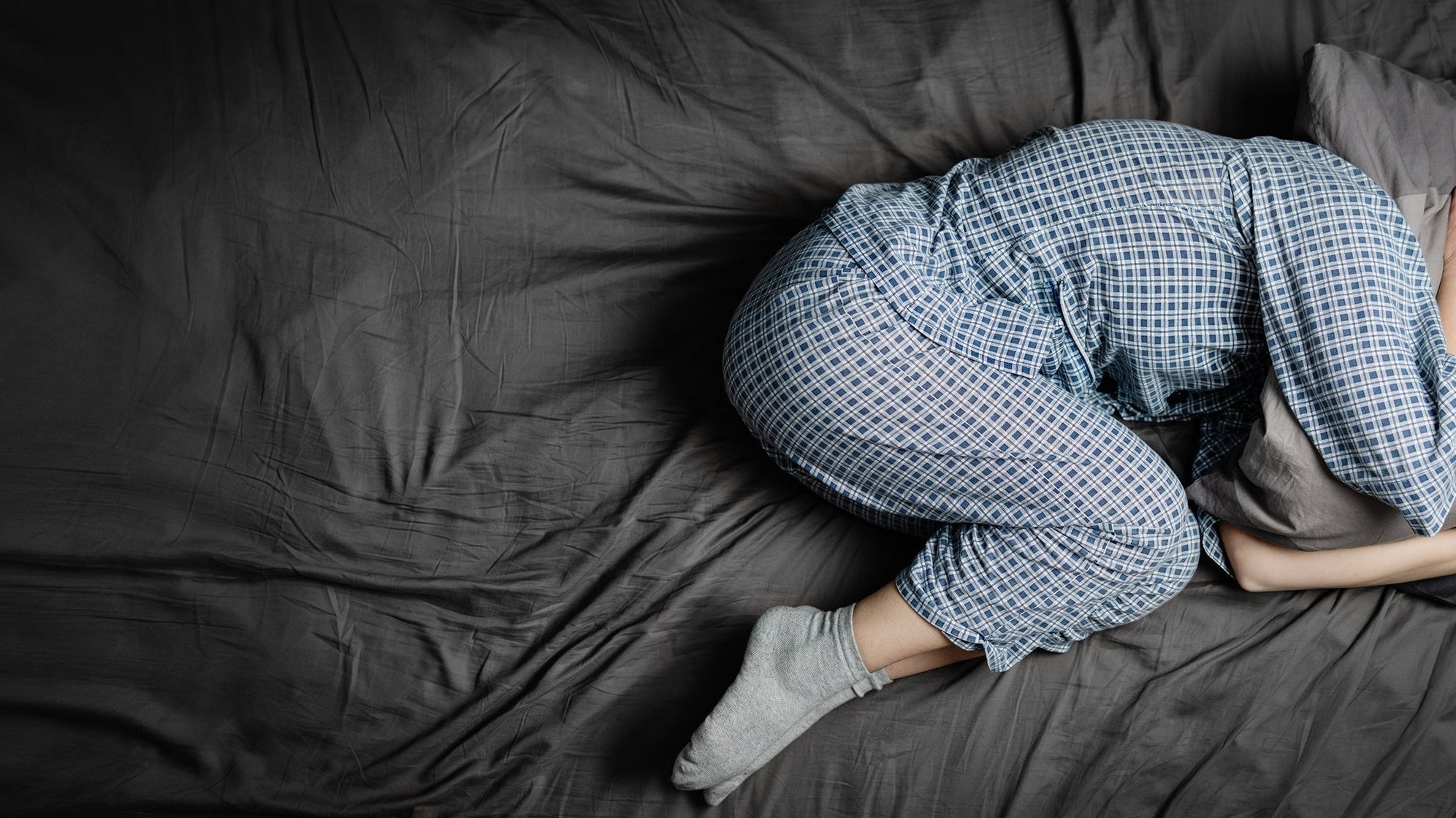 A person curls up in a ball while sleeping. If you're struggling to sleep with shingles, explore out complete guide on why shingles pain is worse at night and how you can get relief.