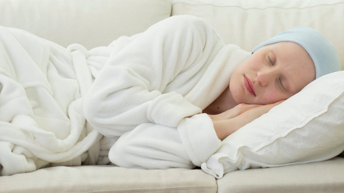 Person sleeping on a sofa in a white robe and light blue head cover.