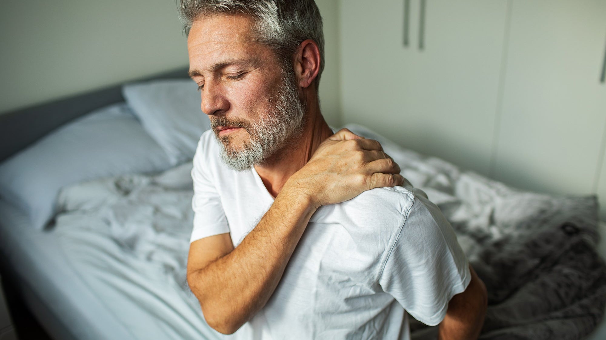 A man with shoulder pain. Frozen shoulder pain waking you up at night? Learn the best sleep positions, proper pillow support, and how to prep before surgery for real, lasting relief.