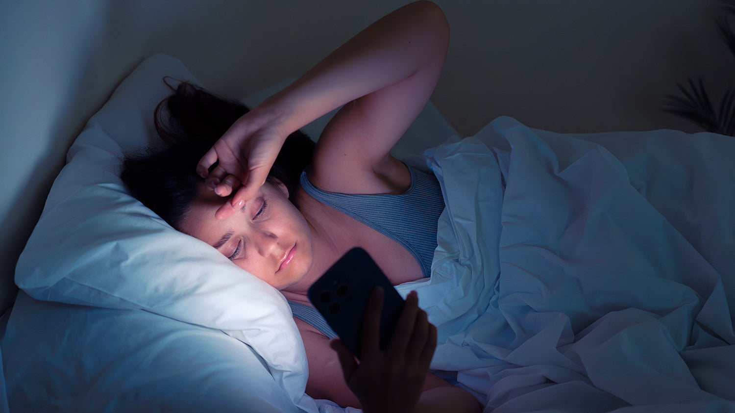 A woman reads her phone in bed. Back sleeping is normally restricted after BBL, but a suspended positioning setup removes the pressure risk. See how to sleep on your back safely during recovery.