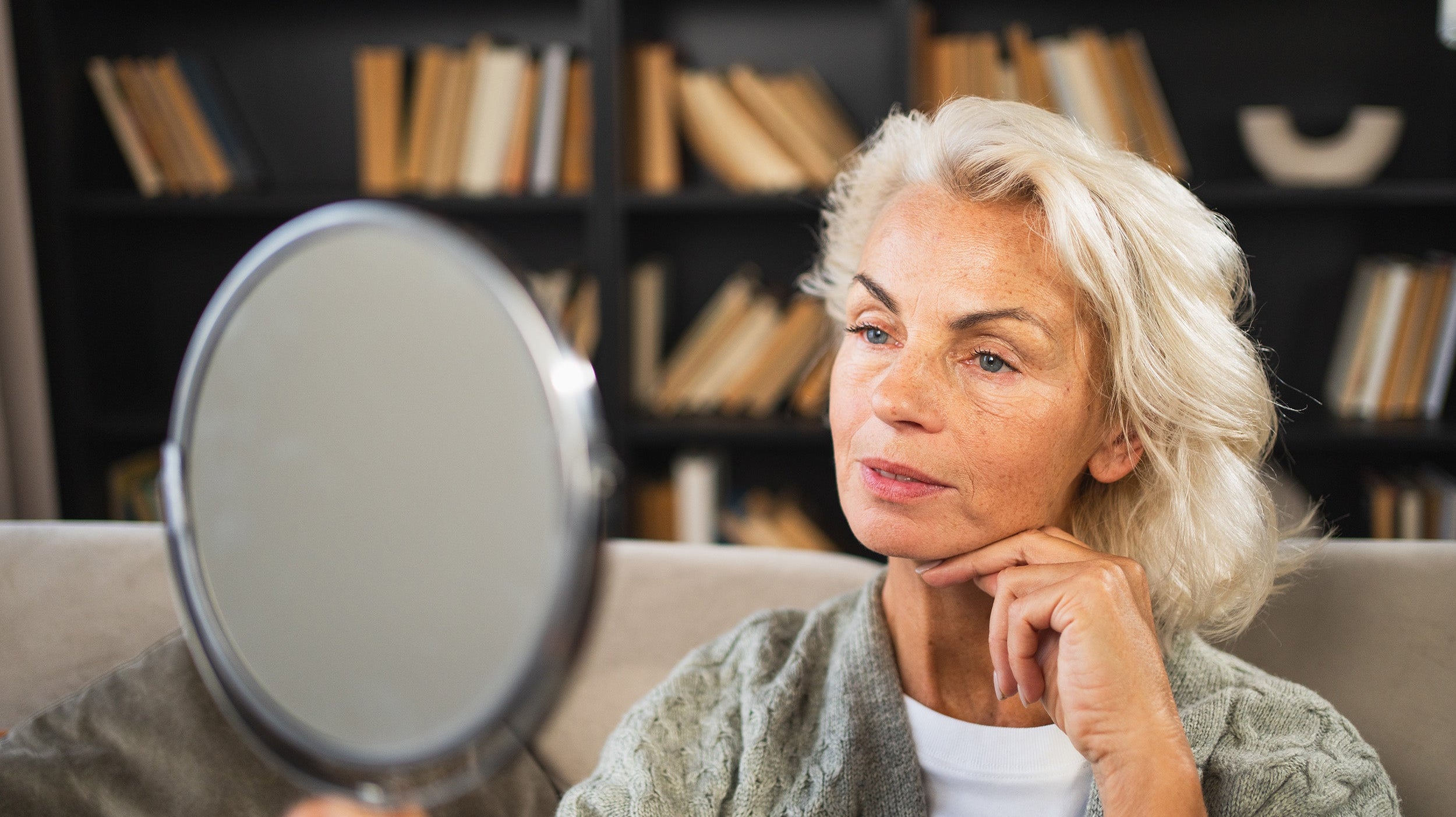 A woman looking in the mirror. Planning a deep plane facelift? Learn how to sleep safely after surgery, how long to stay elevated, and how to set up your recovery space in advance.