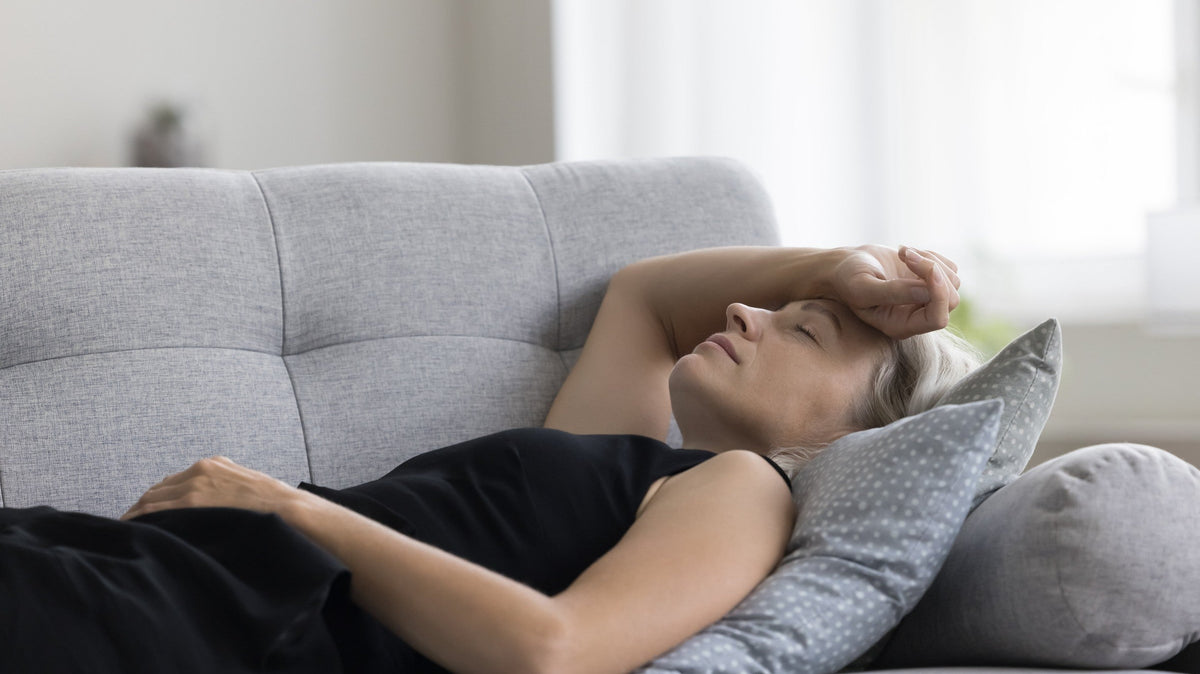 A woman laying on the couch with the back of her hand on her forehead.