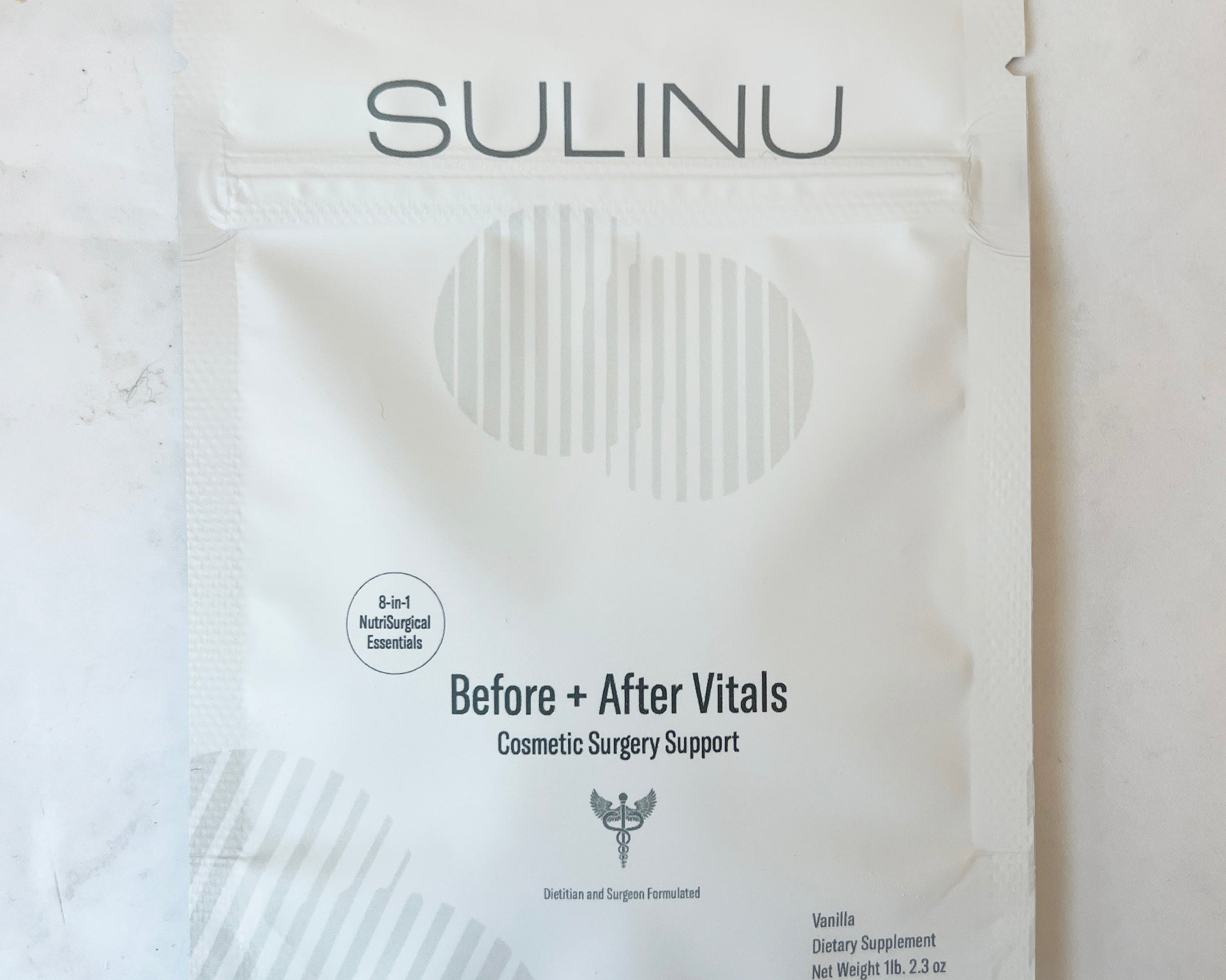 A white Sulinu packet labeled Before + After Vitals Cosmetic Surgery Support, with details about vanilla flavor, 3.2 oz net weight, and B-vitamins, on a light background.