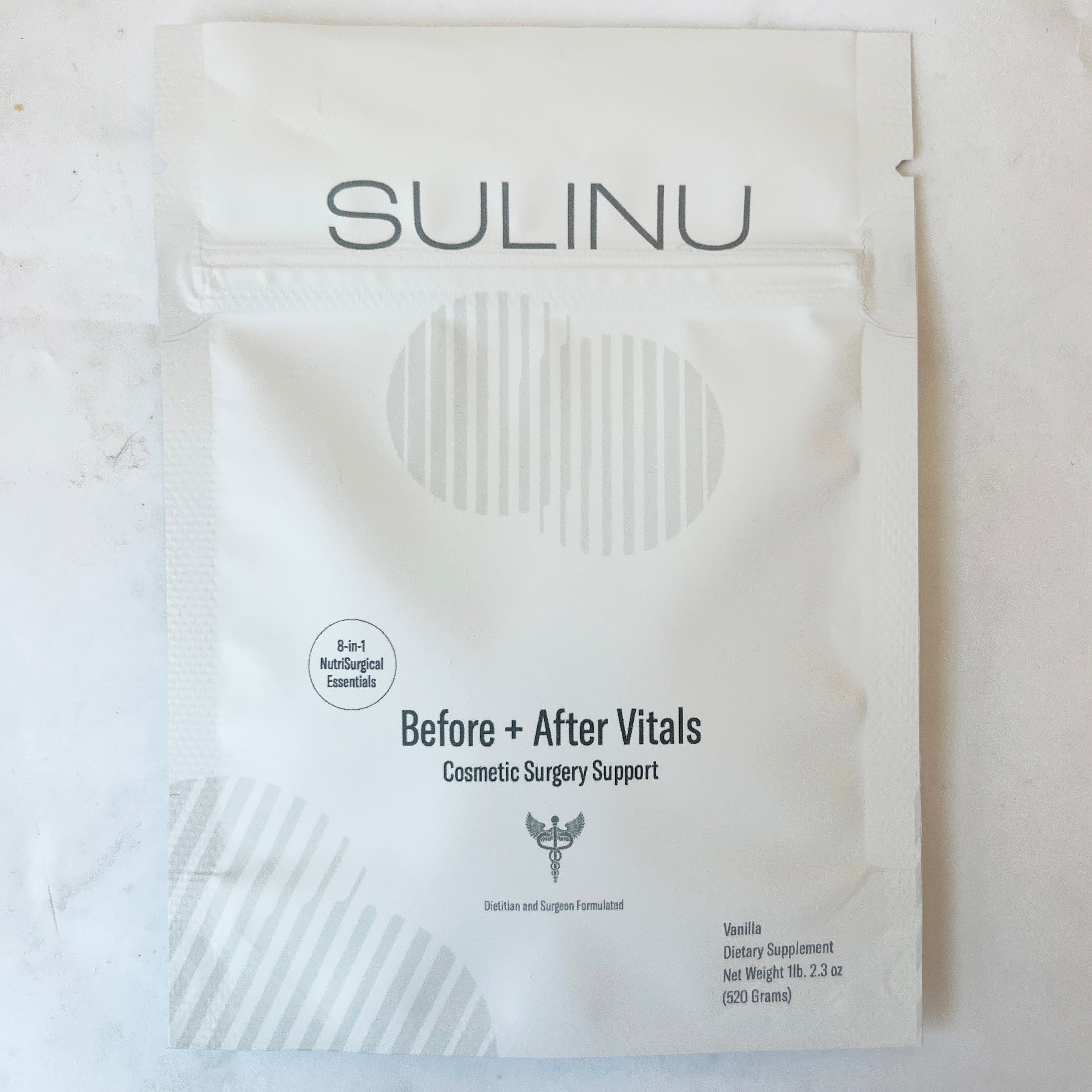 A white Sulinu packet labeled Before + After Vitals Cosmetic Surgery Support, with details about vanilla flavor, 3.2 oz net weight, and B-vitamins, on a light background.