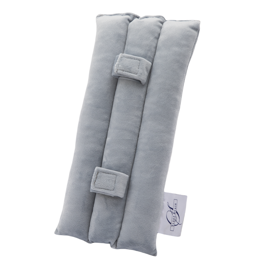 The Seat Belt Pillow is a light gray, rectangular padded fabric cushion designed for chest support. It features three cushioned sections, two rectangular fabric loops, and a small white logo tag on the side. The background is plain white.