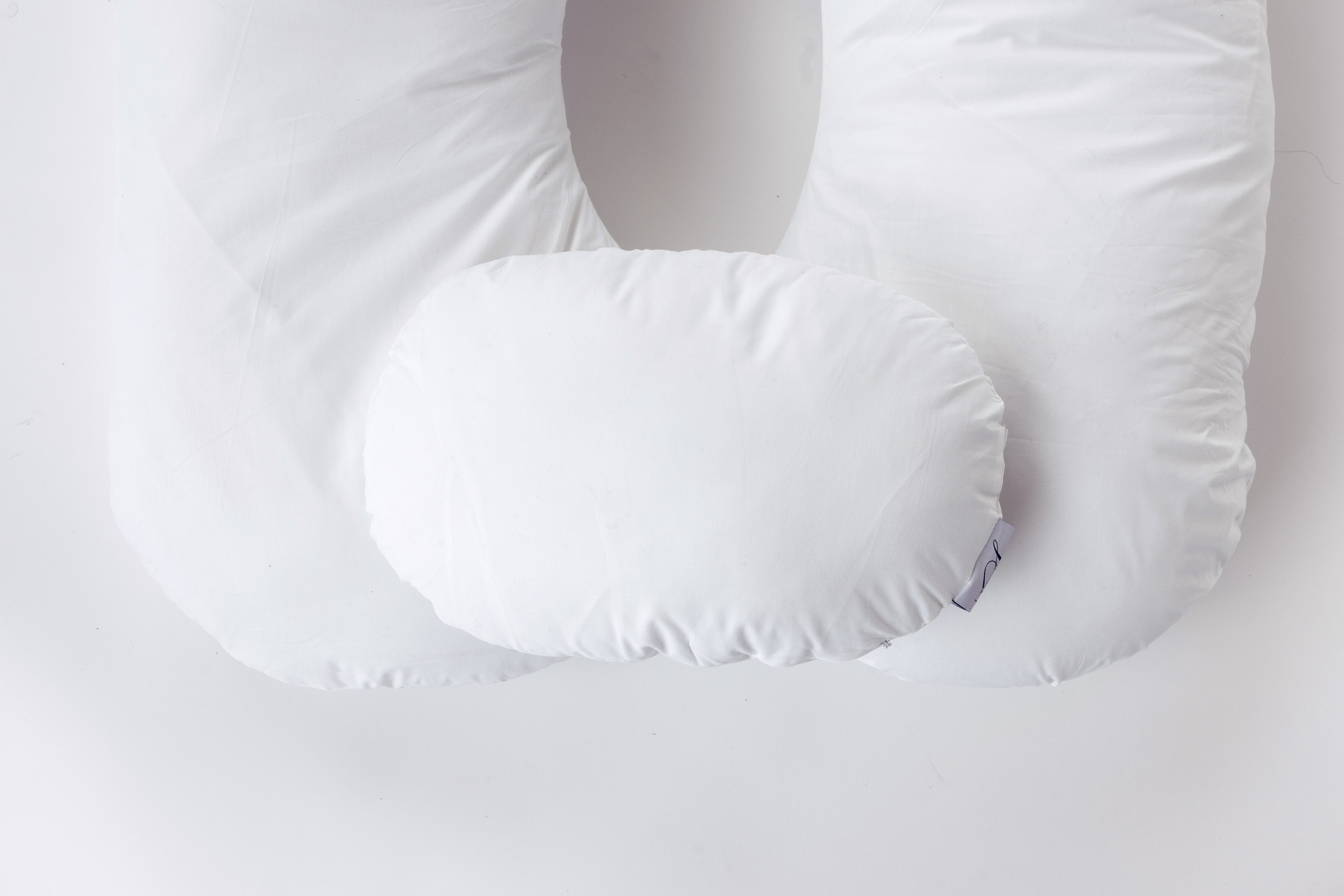 Two white, oval-shaped side pillows from "Two Side Pillows Sold Separately" are displayed atop a contoured body pillow with a washable slipcover, all arranged against a plain white background.