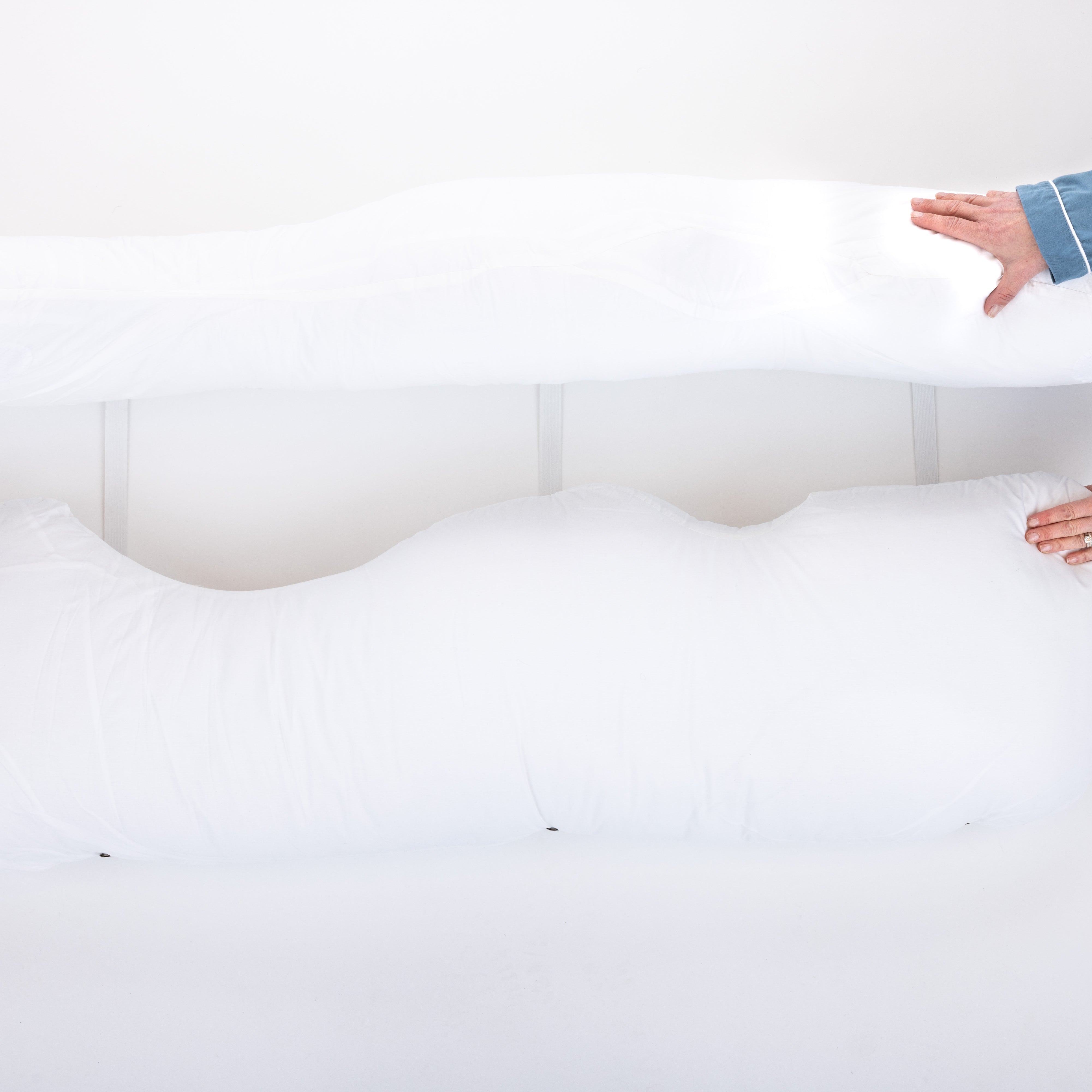 Two hands showing 3 pillow straps attached to side pillows on a light background