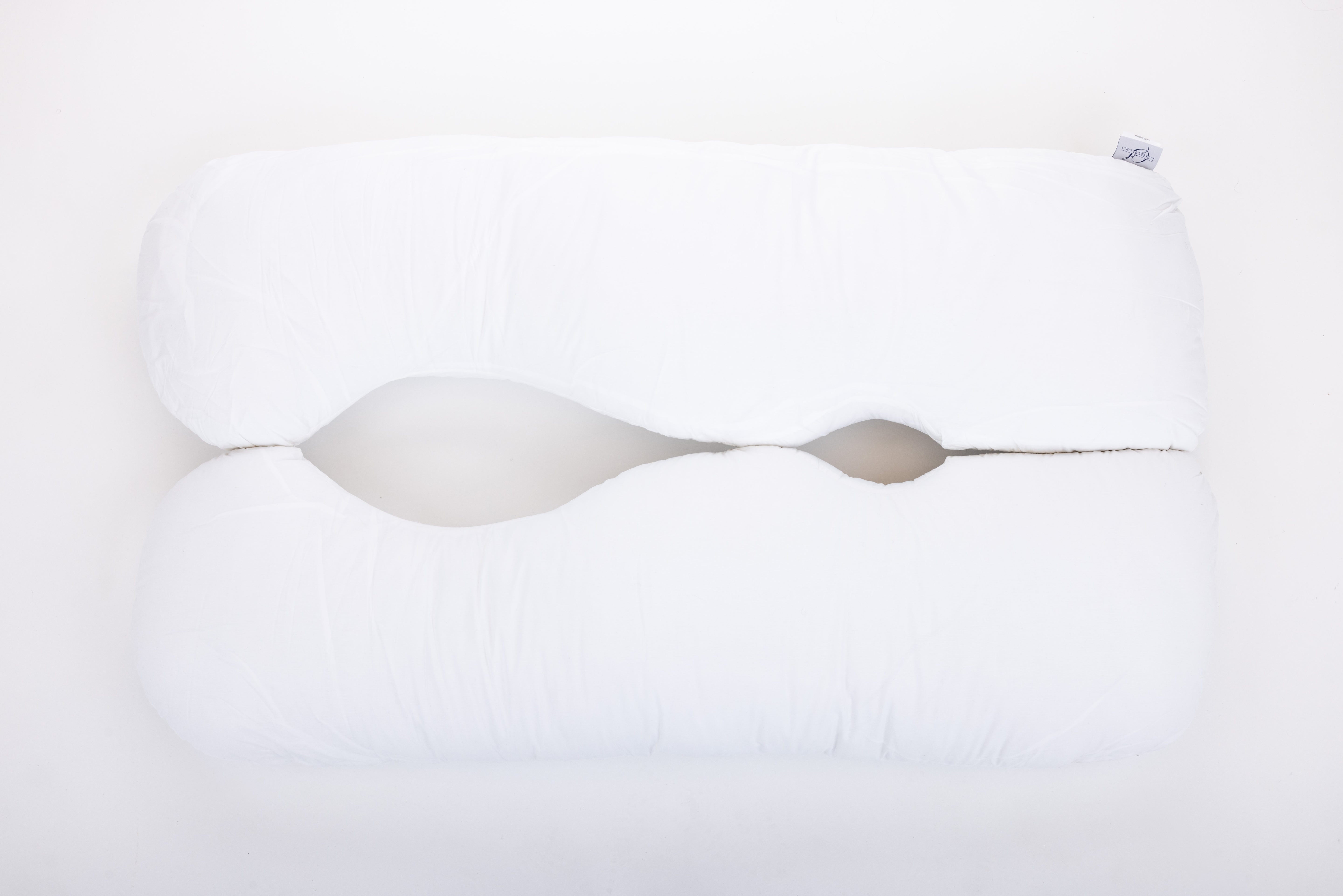 The "Two Side Pillows Sold Separately" is a white, uniquely contoured bedding pillow with a wave-like center cutout, shown on a plain white background.