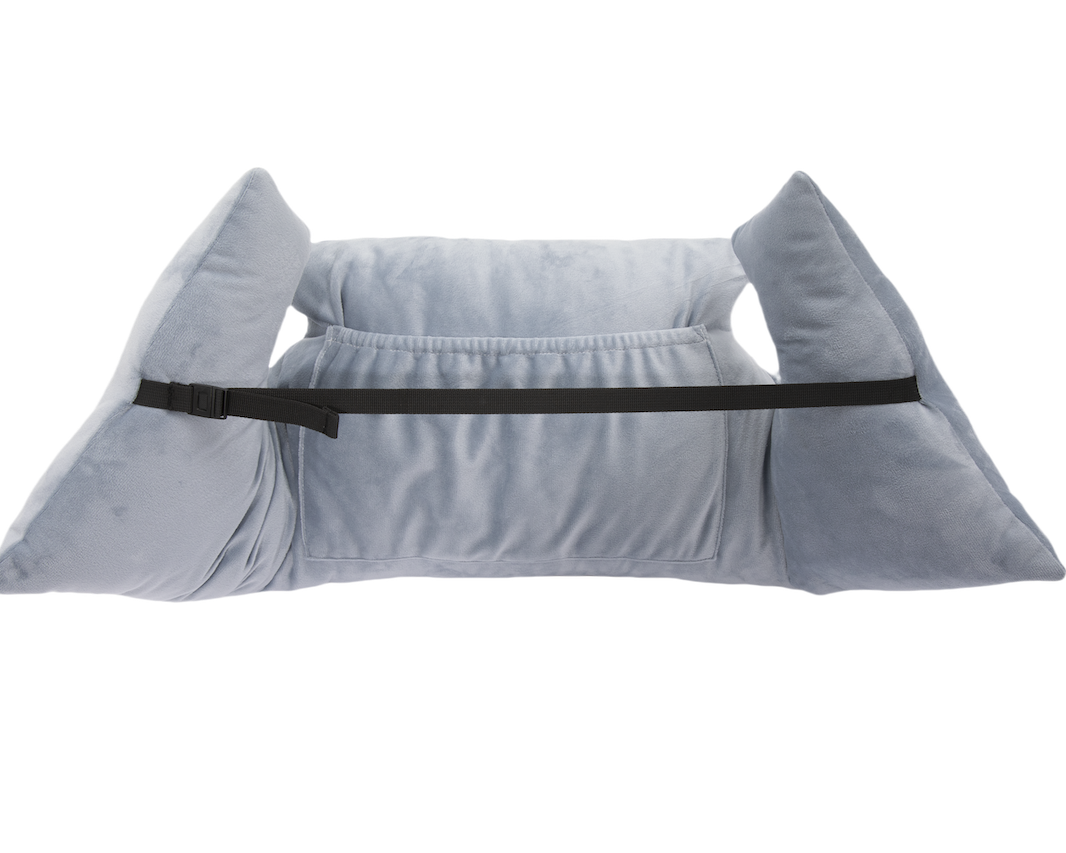 The Chest Pillow is light gray, plush, and features two large side supports, a black adjustable front strap, and a central pocket for positioning and stability after breast surgery. Shown on a white background.