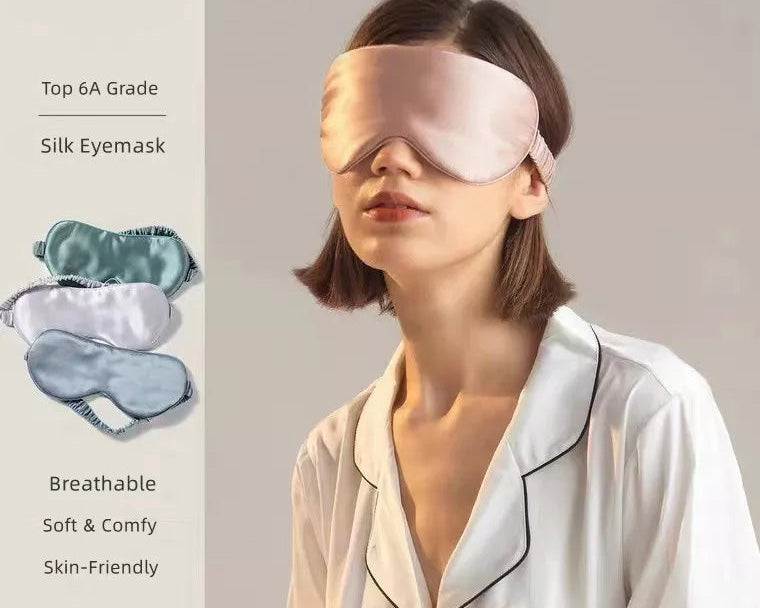 A woman in white pajamas wears a pale pink Mulberry Silk Sleep Eye Mask with Silk Covered Elastic Strap, standing against a neutral background. Eye masks in various colors are displayed nearby, with text noting their soft, breathable qualities.