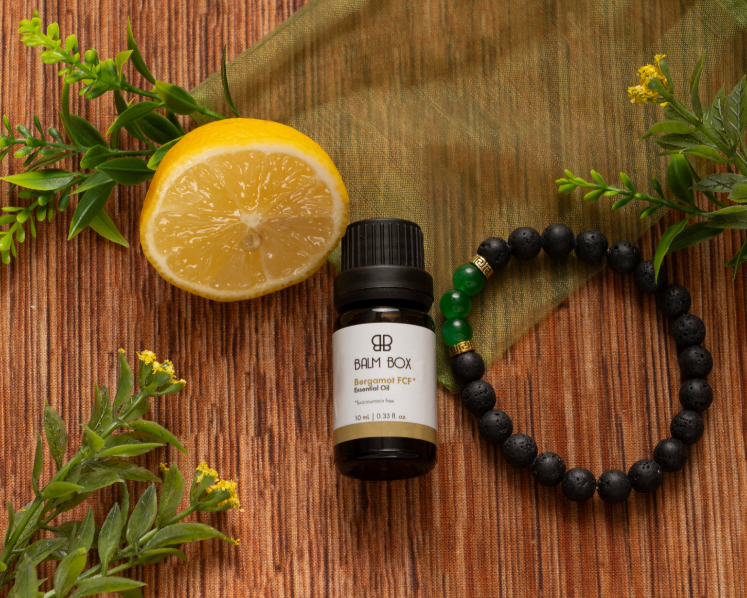 The Best Mastectomy Care Package features essential oil, a beaded bracelet, and a lemon half on a wooden surface with green leaves and fabric—thoughtful details for a breast cancer gift.