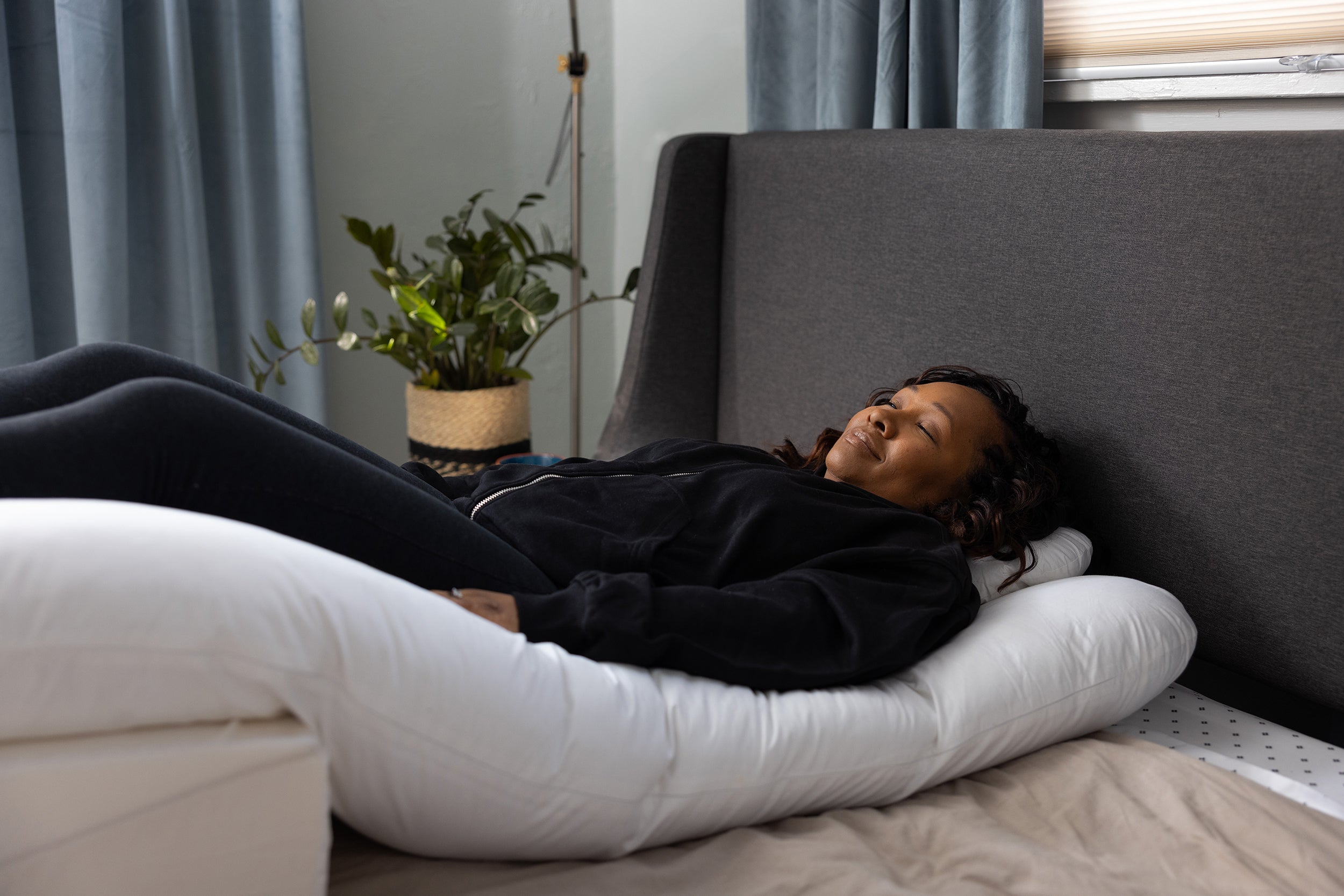 A woman rests in a bed, using the Sleep Again Pillow System and its double wedges to alleviate pain the lower back.