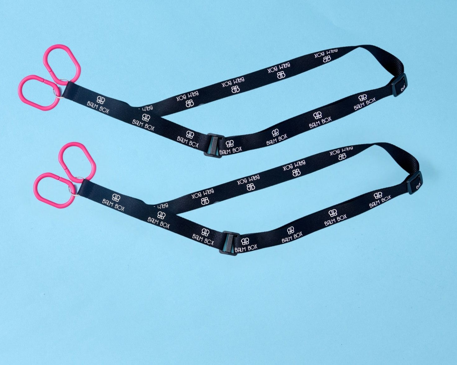 Two black straps with white text and logos, each ending in a pair of red plastic handles, are laid out on a light blue background—perfect for use as the Surgical Drain Holder.