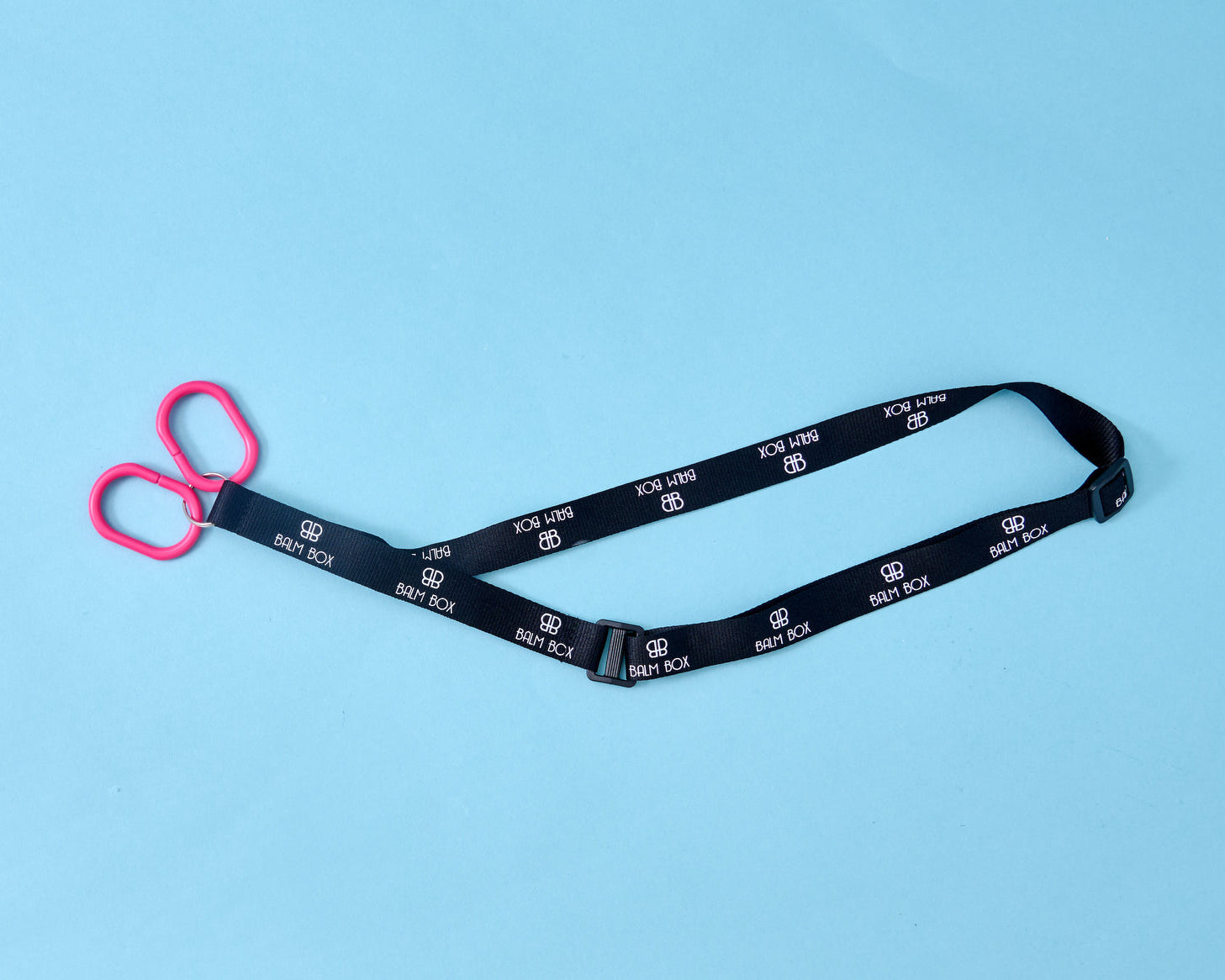 A pair of pink-handled safety scissors attached to a black lanyard with white BABY BOK logos, placed on a light blue background—perfect for use alongside the Surgical Drain Holder.