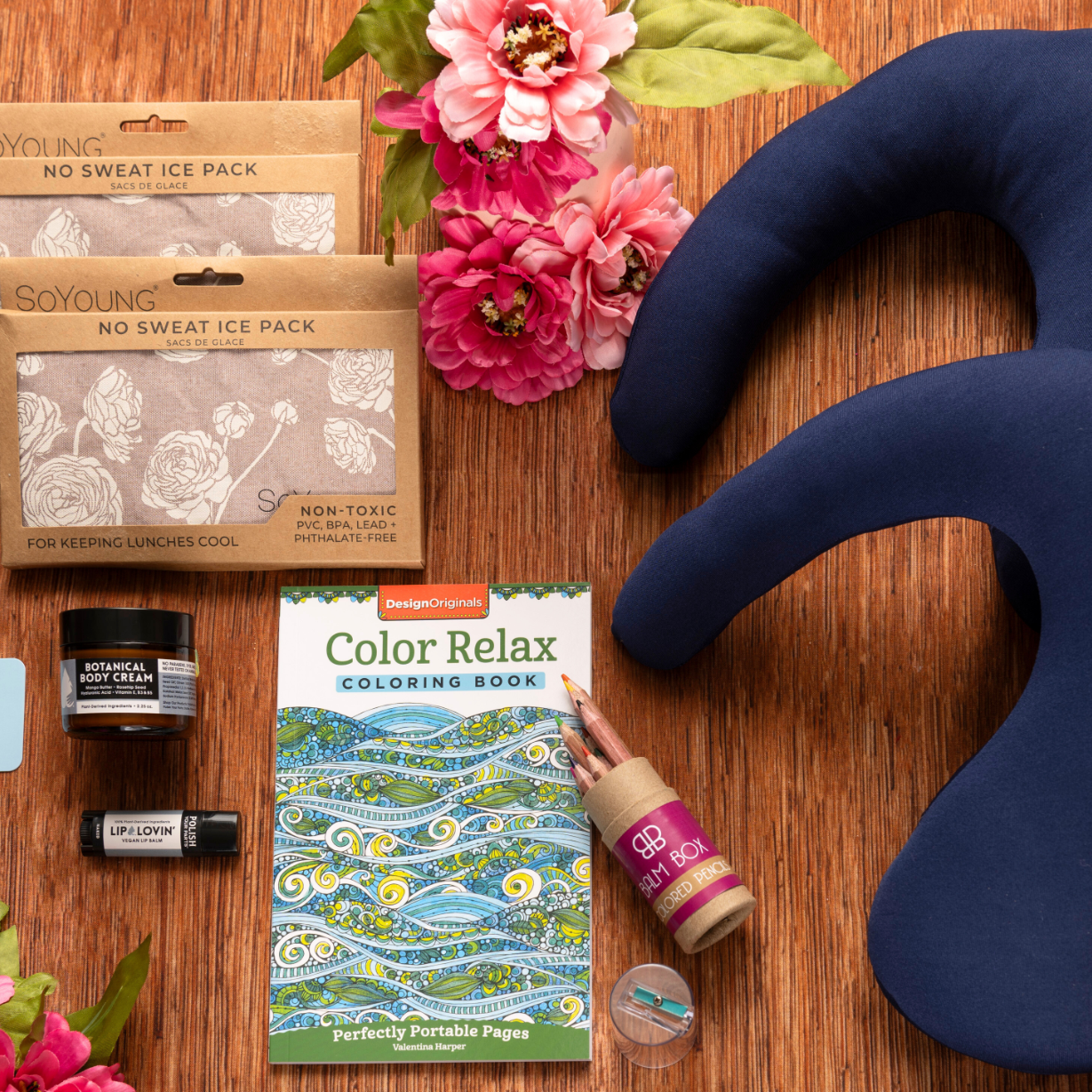 The Best Mastectomy Care Package features navy blue cushions, ice packs, a coloring book, colored glue, a candle, lip balm, pink artificial flowers, and green leaves—ideal for relaxation and self-care after surgery.