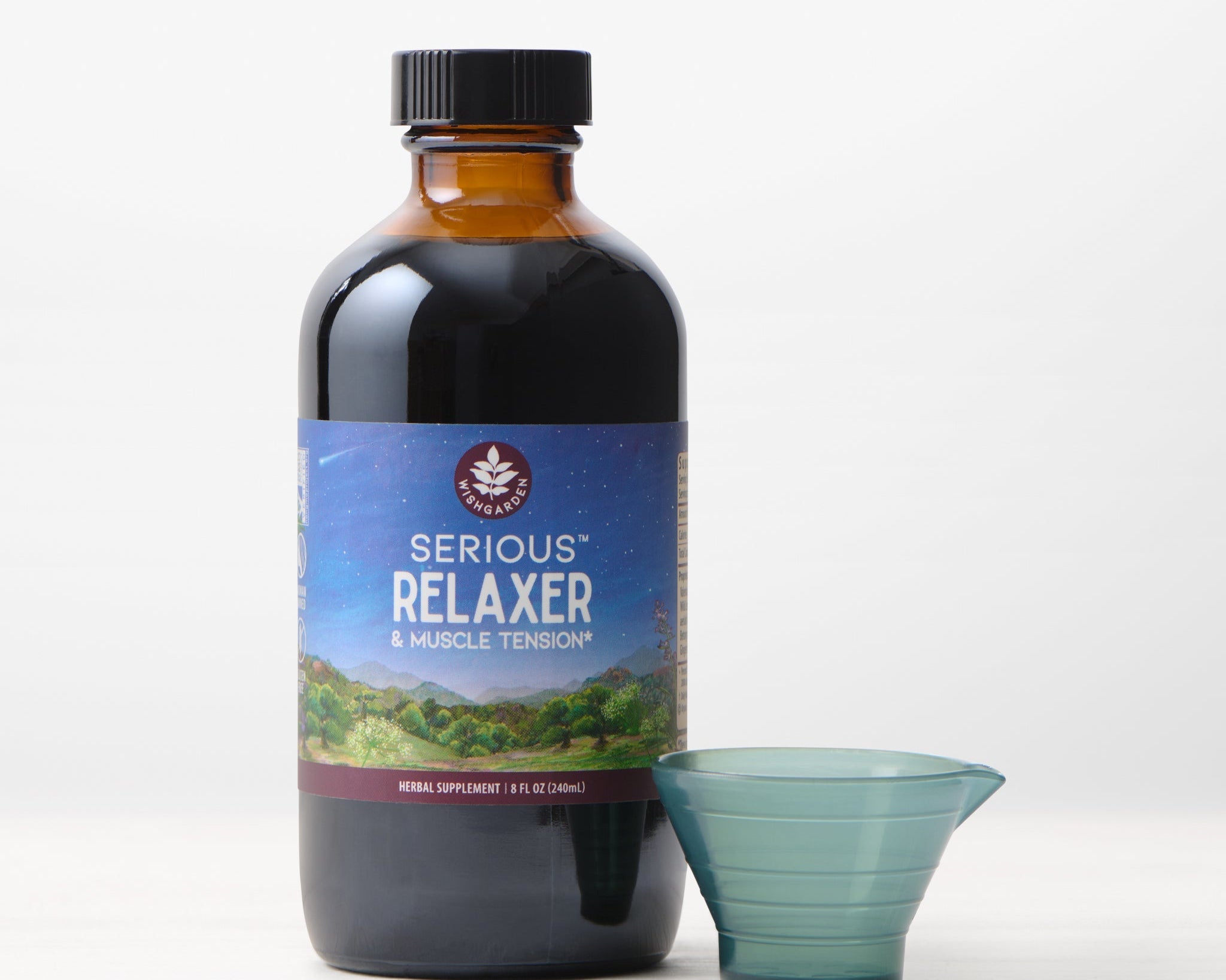 A dark glass bottle labeled "Serious Relaxer & Muscle Tension" stands next to a small, empty plastic measuring cup on a white surface, providing muscle tension relief and extra stress support.