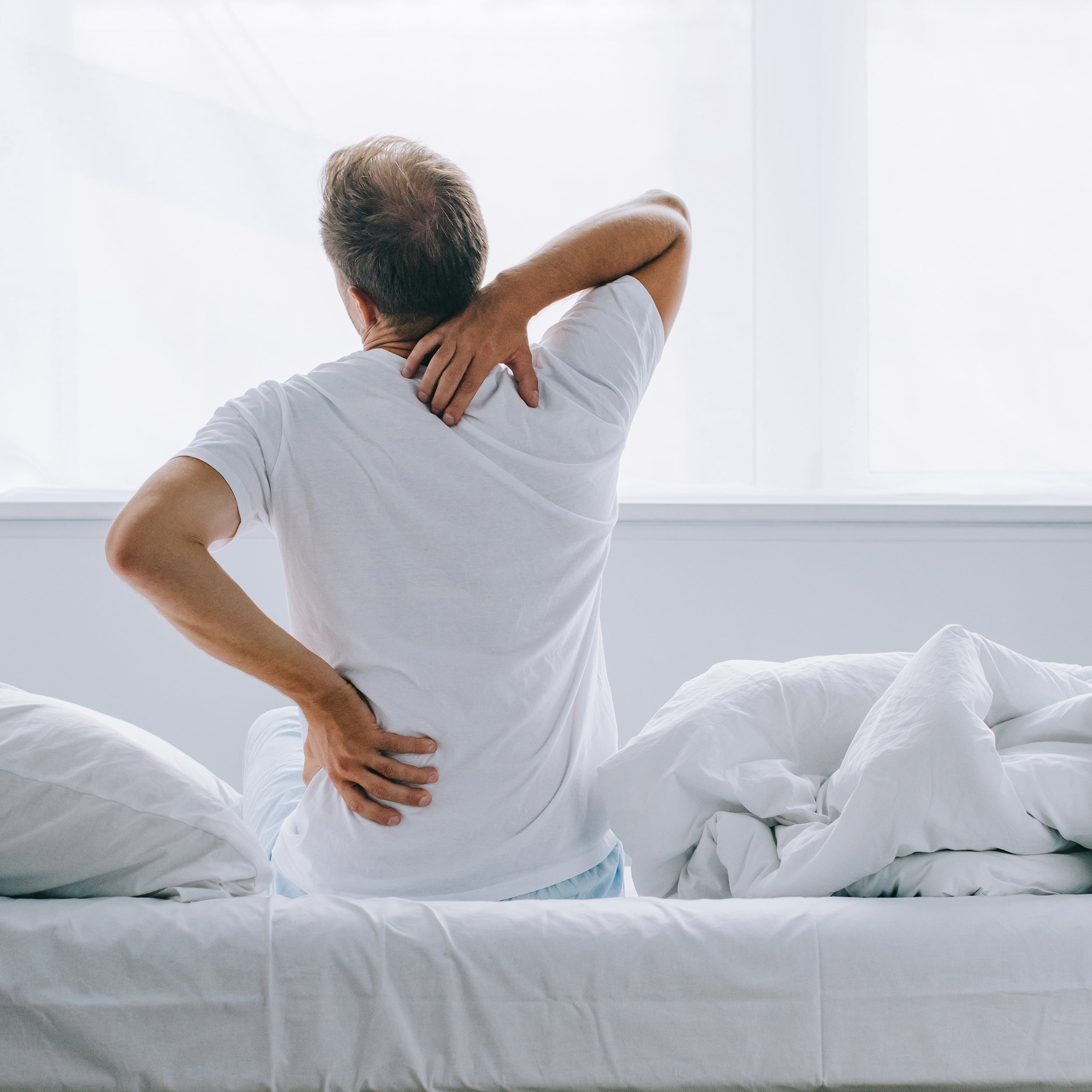 A man clutches his back and neck after waking up in pain. Sleep Again Pillows offers the best pillows for back pain to help relieve the symptoms of acute or chronic back pain from ongoing conditions or injuries.