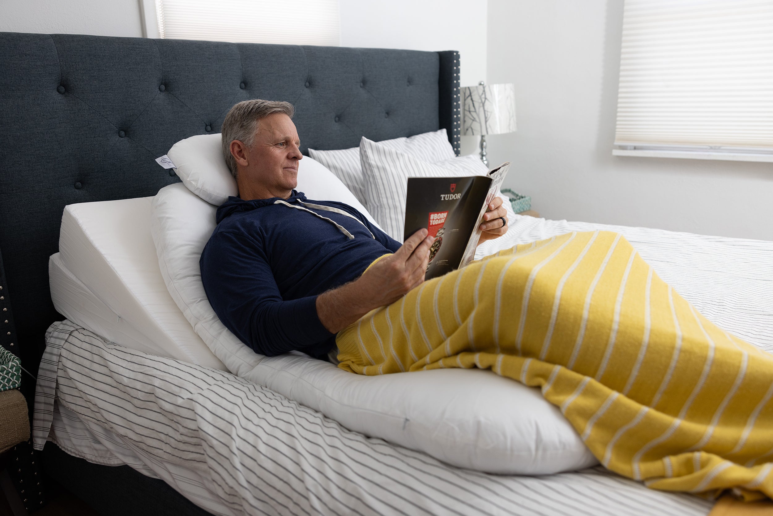 A man rests in bed on the Sleep Again Pillow System, a five-pillow system combining two wedges, two body pillows, and a neck pillow to provide relief and assist in the recovery from a wide variety of surgeries and chronic conditions.