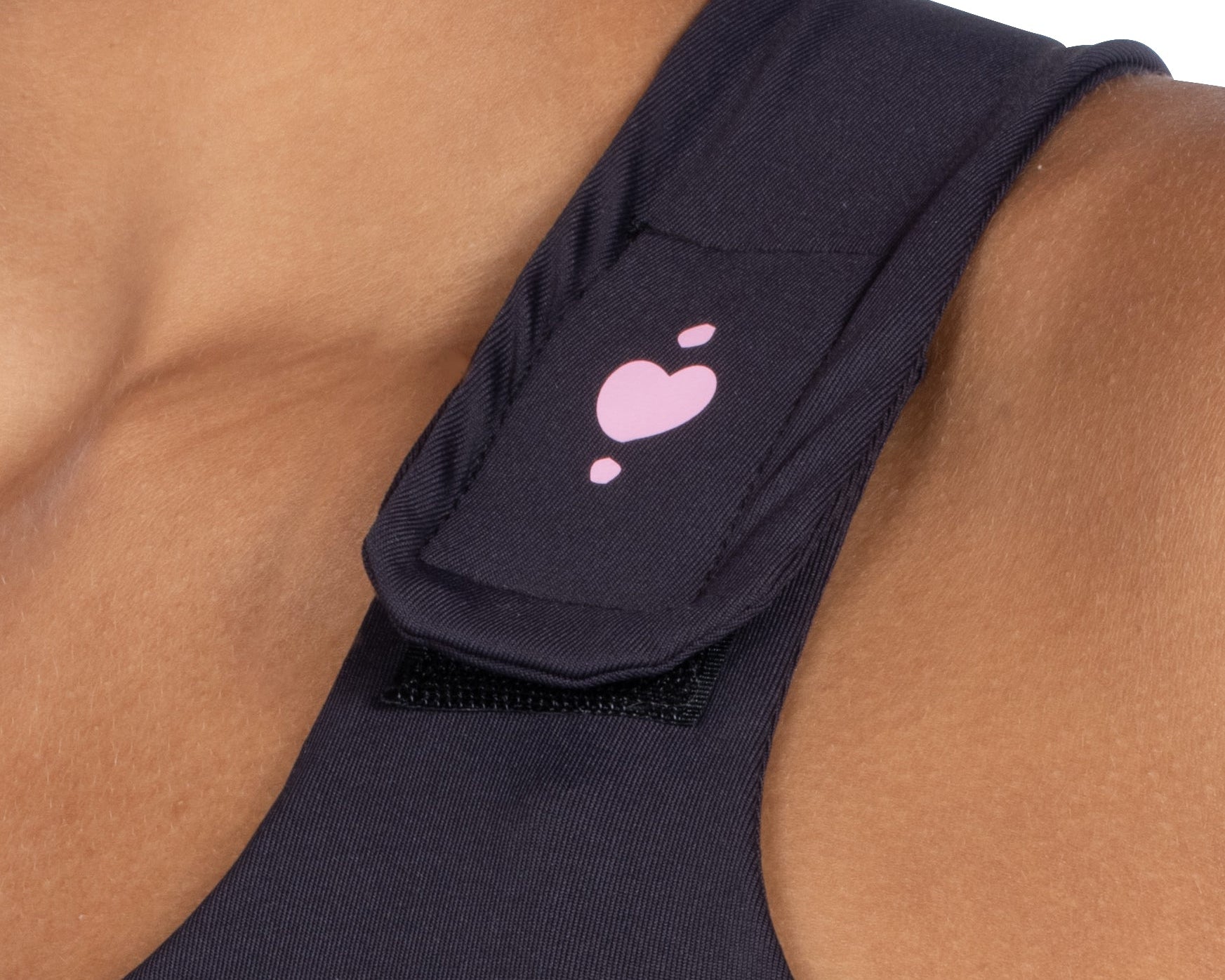 Close-up of a person’s shoulder wearing the Serena Post-Surgical Bra in a dark color, featuring a strap with a pink heart and three small pink dots. The strap is part of this reconstructive surgery garment.