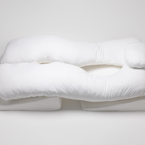 The Sleep Again Pillow System is a large, white U-shaped body pillow with a headrest, offering ergonomic support for arms, legs, and head. HSA and FSA eligible, it rests on a white surface for optimal comfort.