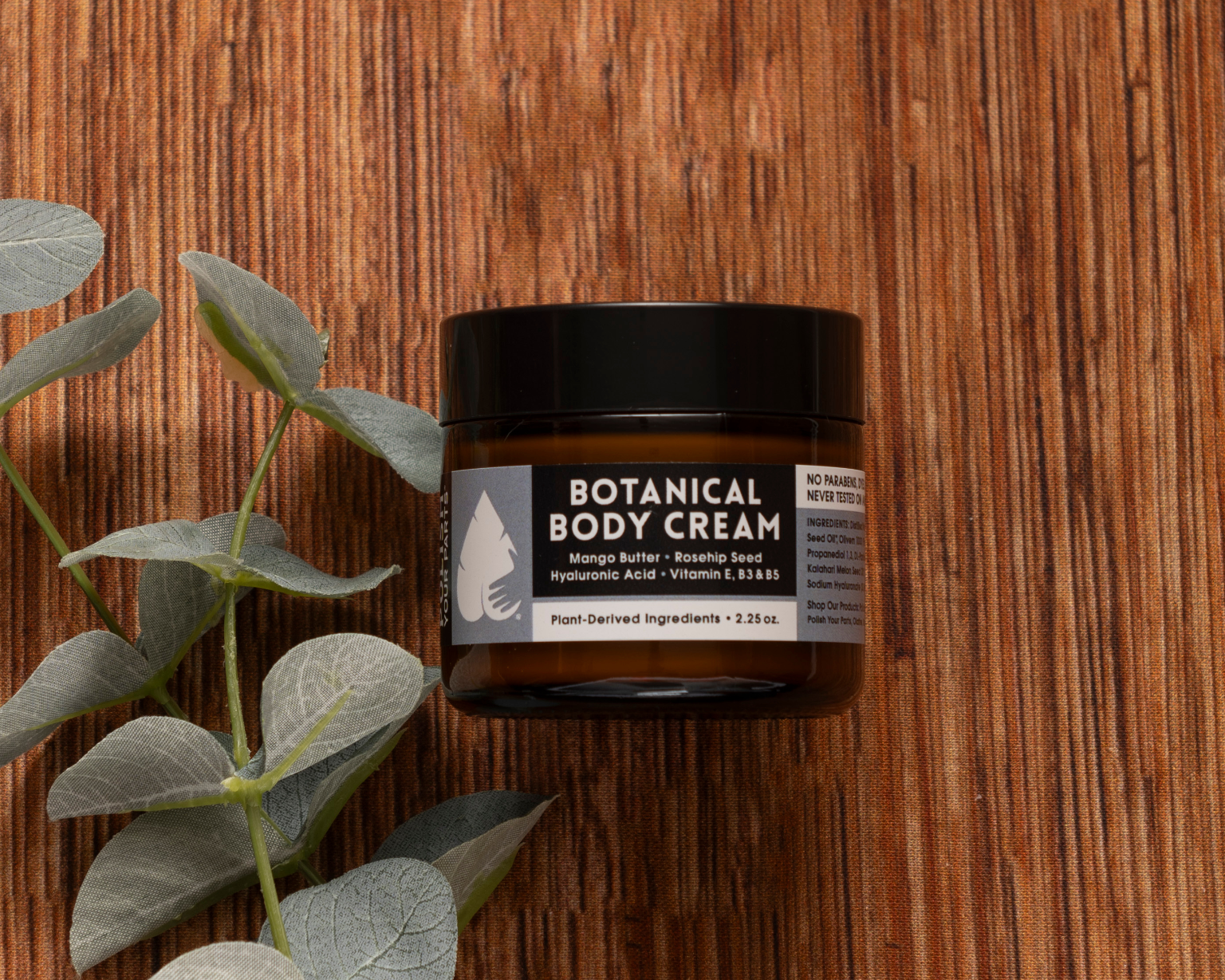 The Best Mastectomy Care Package features a Botanical Body Cream with mango butter, rosehip seed, hyaluronic acid, and vitamin E—perfect for soothing care, beautifully presented beside silver-green eucalyptus on a wooden surface.