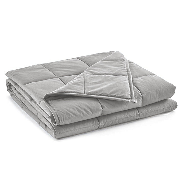 The Pillowtex Weighted Blanket, in light gray with a soft texture, is shown neatly folded on a white background. A corner is turned over to reveal its thickness, detailed stitching, and premium glass bead filling.