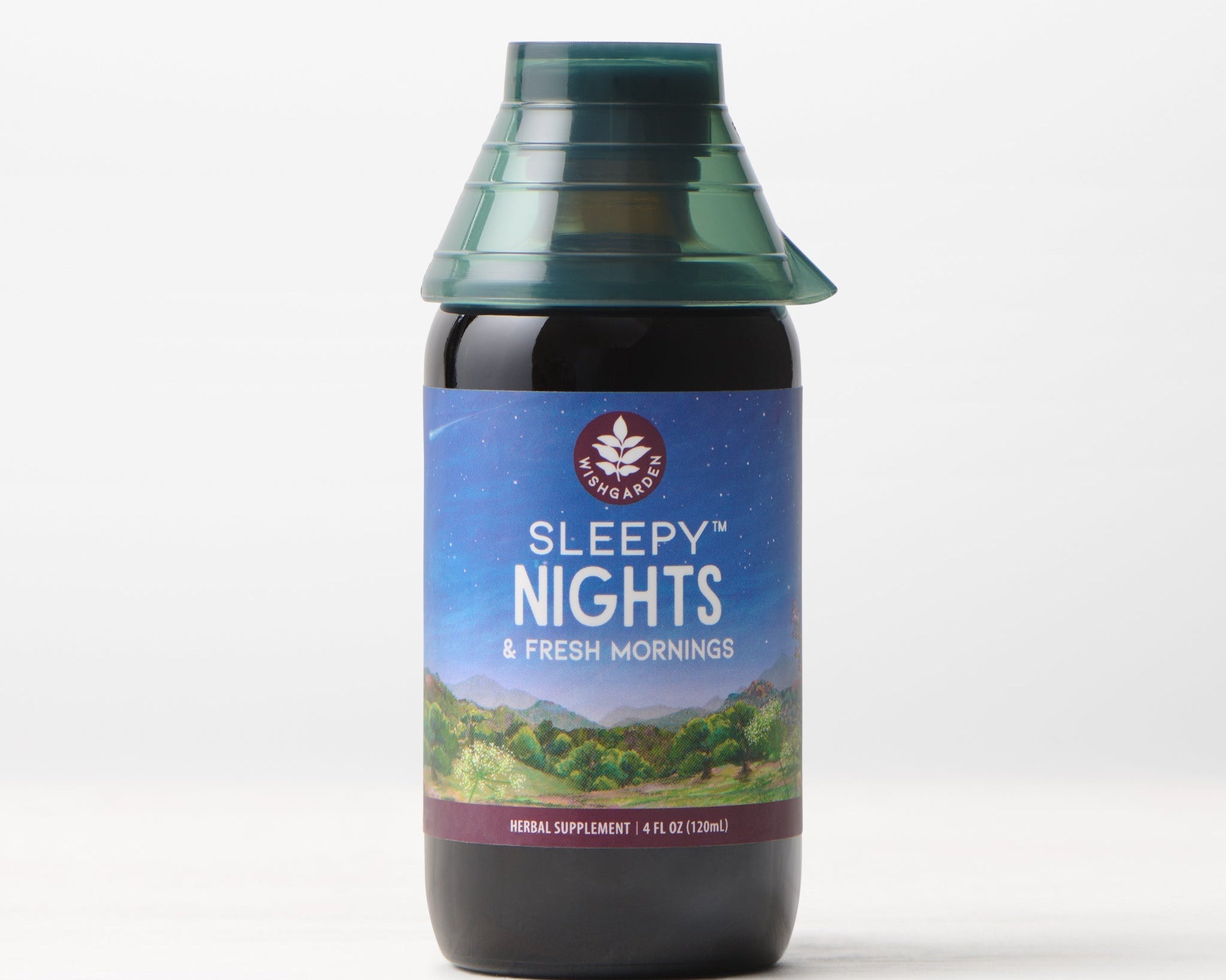 A bottle of Sleepy Nights & Fresh Mornings sleep supplement sits on a light surface, displaying a scenic label with mountains, sky, and stars, and is topped with a green, cone-shaped cap.
