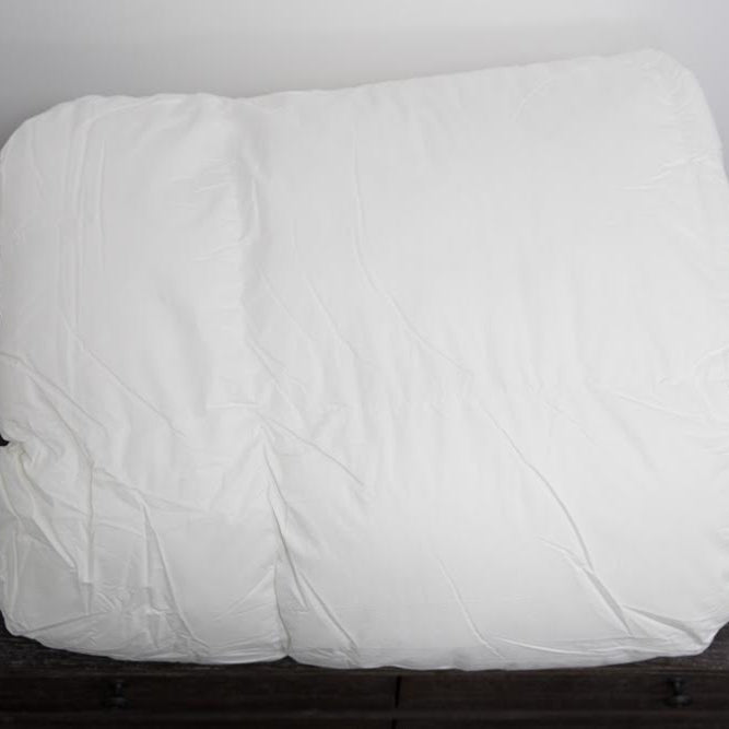 A fluffy white pillow rests on a dark wooden surface against a white wall, perfectly paired with The Twovet Comforter | Couples Comforter "The Duvet for Two" for cozy, hypoallergenic comfort.