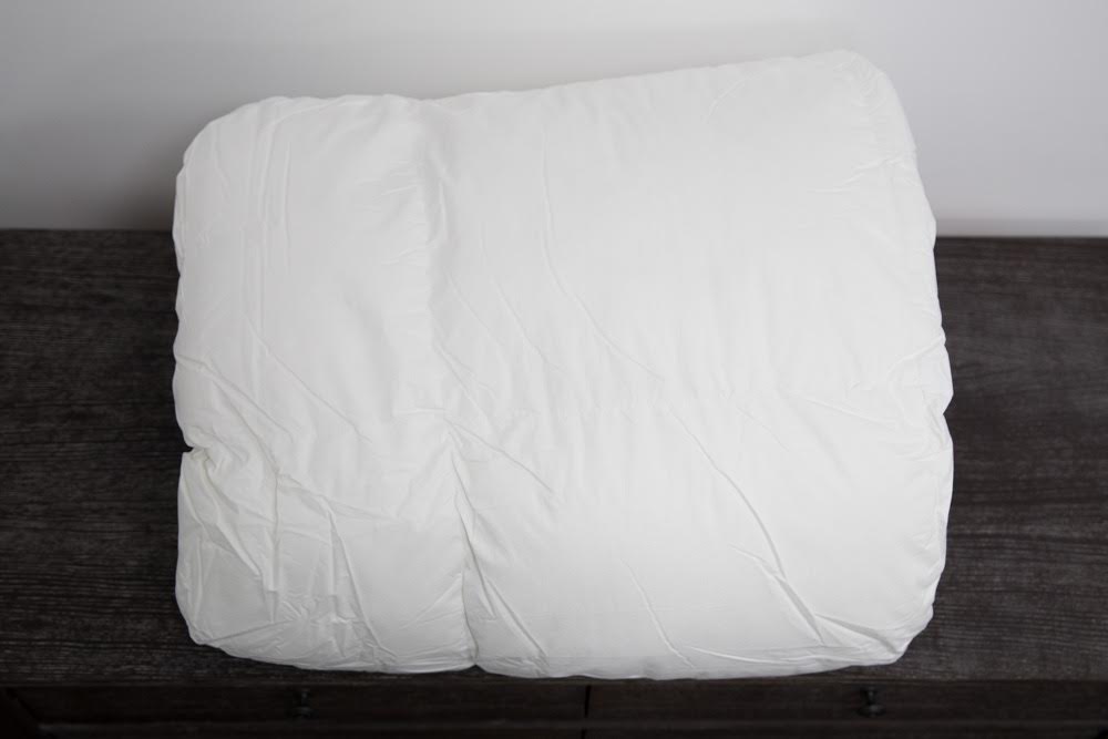 A fluffy white pillow rests on a dark wooden surface against a white wall, perfectly paired with The Twovet Comforter | Couples Comforter "The Duvet for Two" for cozy, hypoallergenic comfort.