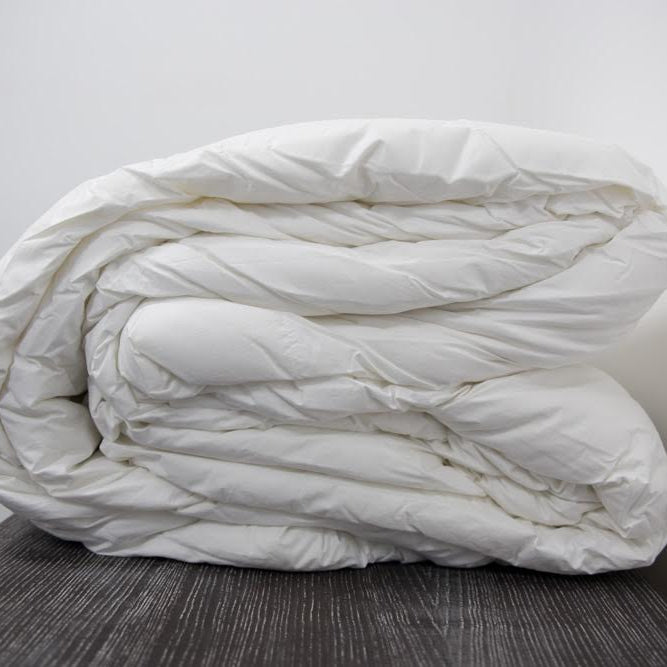 The Twovet Comforter | Couples Comforter "The Duvet for Two," an eco-friendly and hypoallergenic comforter, is neatly folded on a dark wooden surface against a plain white wall.