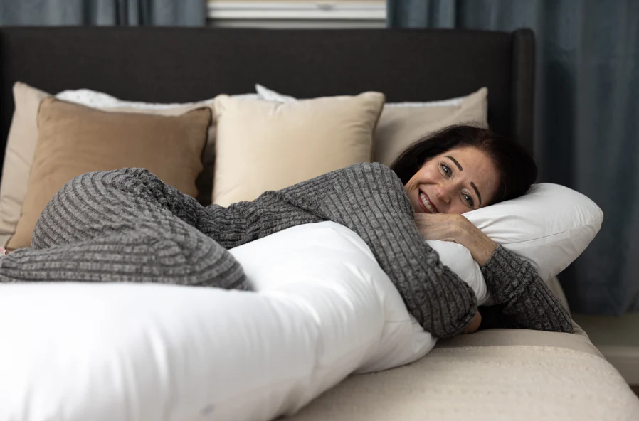 A woman hugs a long body pillow, part of the Sleep Again Pillow System. 