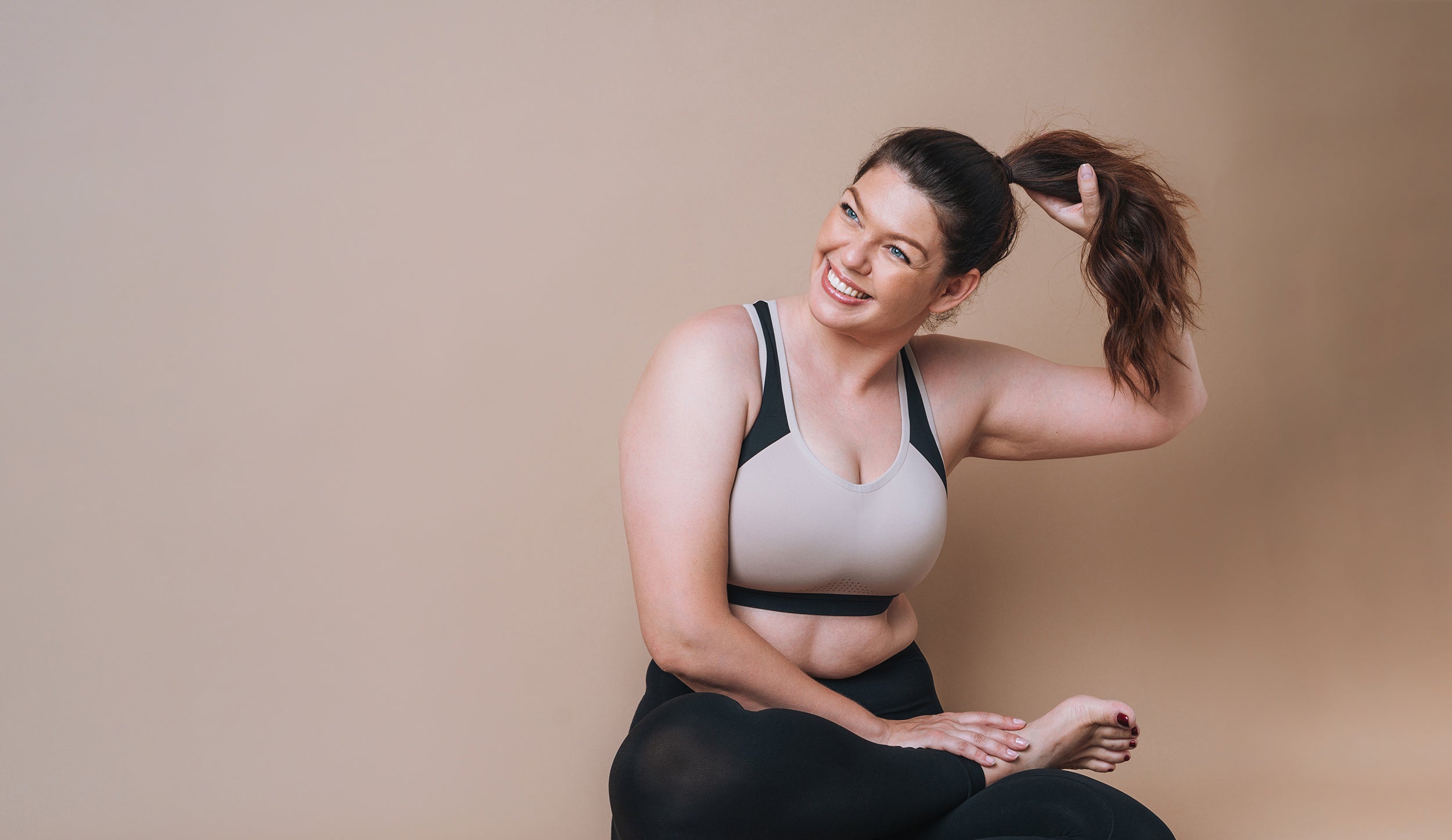 A fit woman sits in a yoga studio. Which sleep position is best for large breasts? Learn more in our complete guide.
