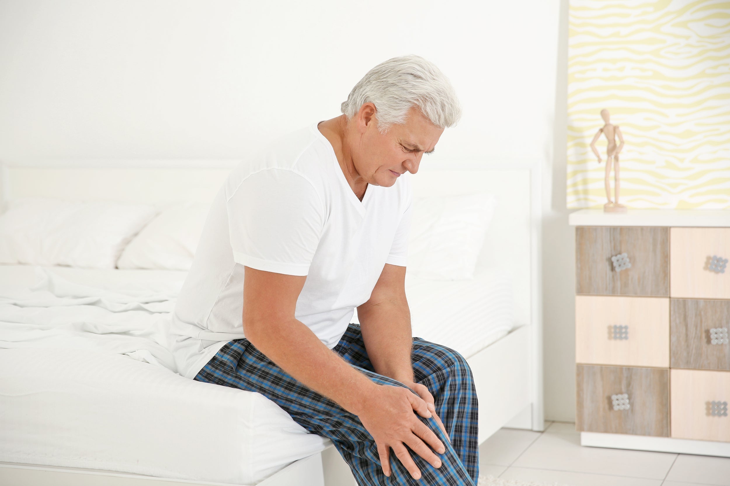 An older man clutches his leg in pain. If you're struggling to sleep with PAD (peripheral artery disease) check out our complete guide on the circulation connection between elevated sleeping and PAD.