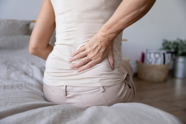 A woman clutches her back in pain. Discover the best sleeping positions for sciatica relief. Learn elevation angles, pillow placement, and positioning strategies that reduce nerve pain tonight.