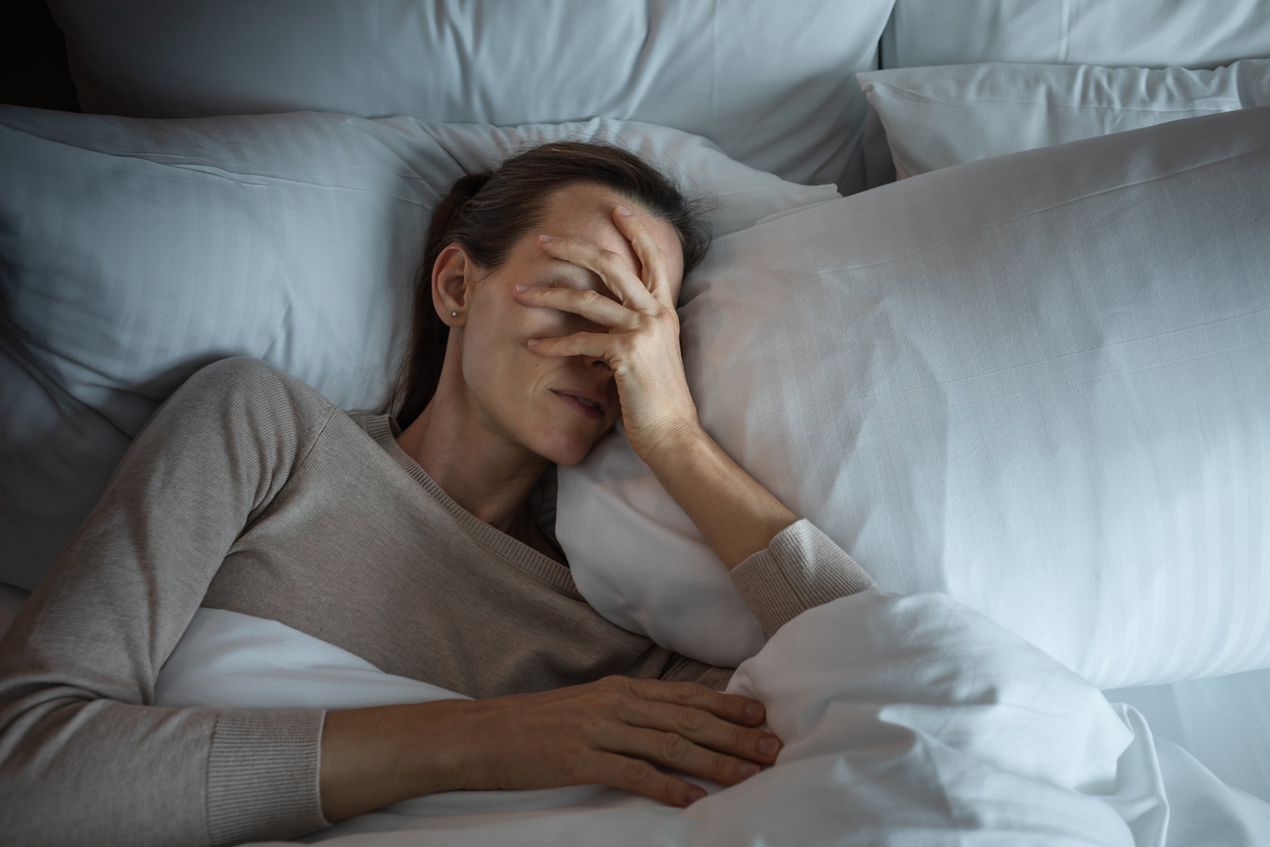 A woman struggles to sleep. Learn more on how to stop rolling over onto your back following breast surgery in our complete guide.