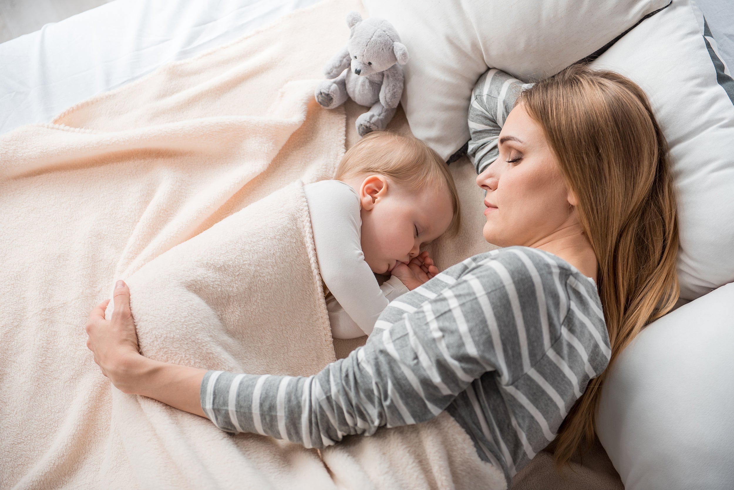 A mother and her newborn baby rest in bed. Sleeping after a C-section can be challenging. Learn more about real solutions for how to sleep after C-section in our new mom survival guide.
