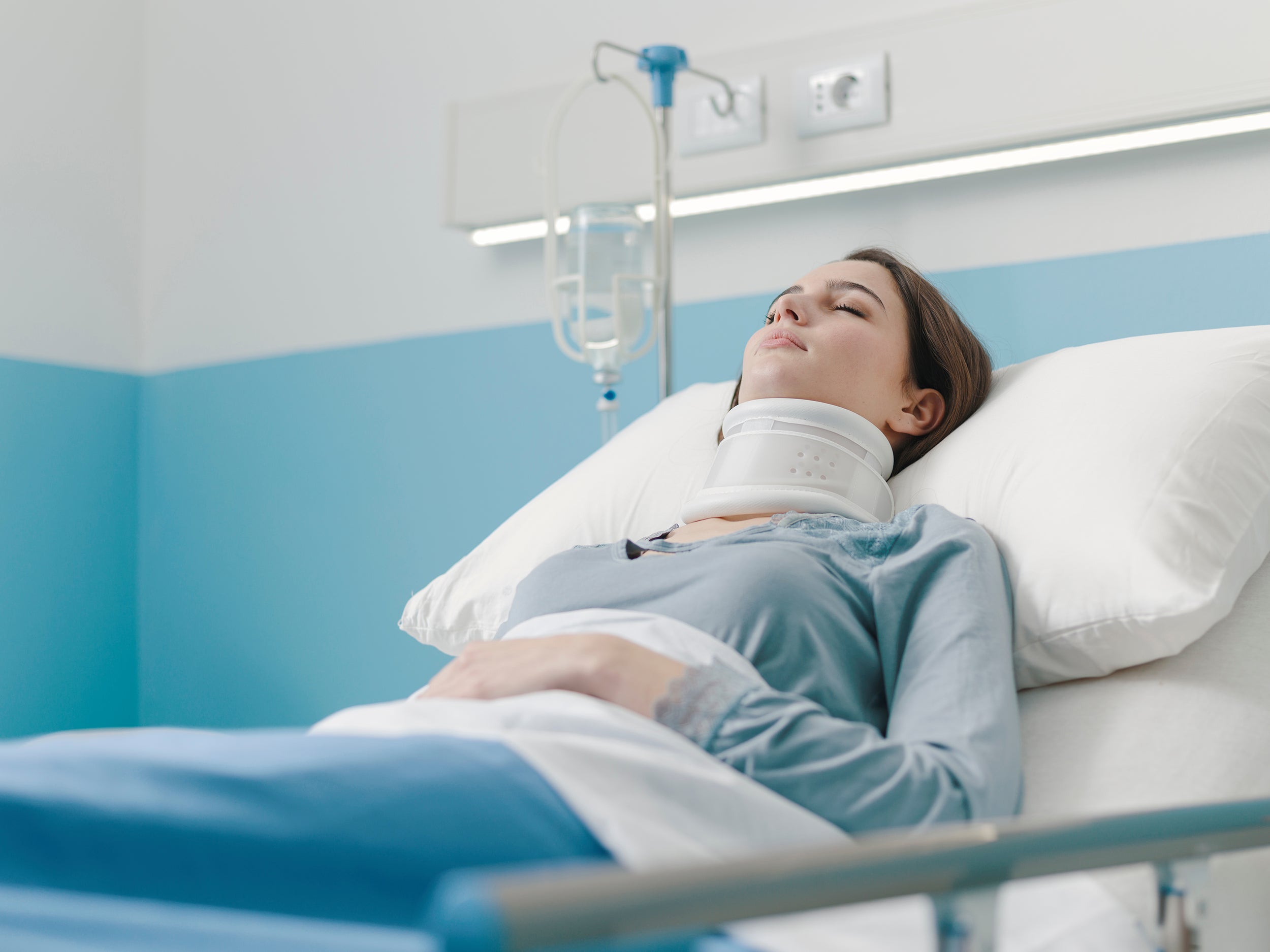 A woman rests in a hospital bed following neck surgery. Learn more about how to get the rest and sleep you need after cervical neck surgery in our comprehensive guide.