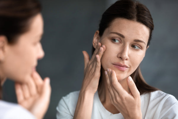 A woman looks at her face in the mirror. Elevated back sleeping at 30–45 degrees is the key to managing swelling after genioplasty. Here's how to maintain it all night without stacked pillows.